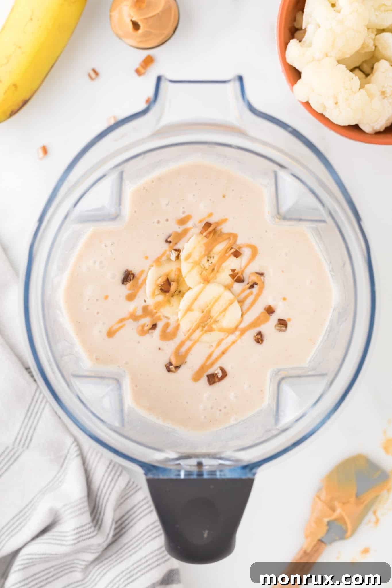 A freshly blended cauliflower smoothie in a high-speed blender, ready to be poured into glasses, with a swirl of peanut butter on top.