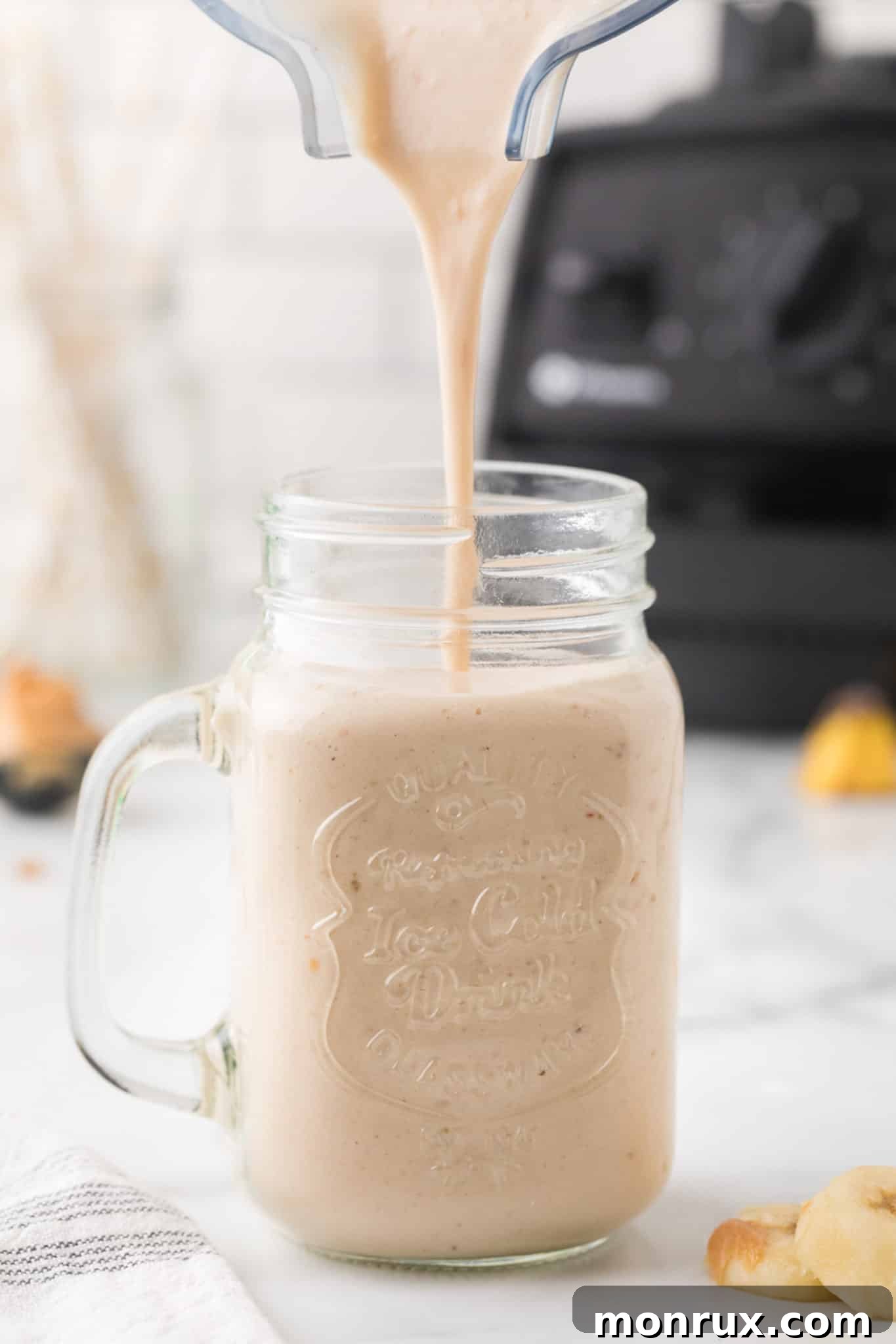 Smoothie being poured from a blender pitcher into a clear glass, showing its creamy texture.