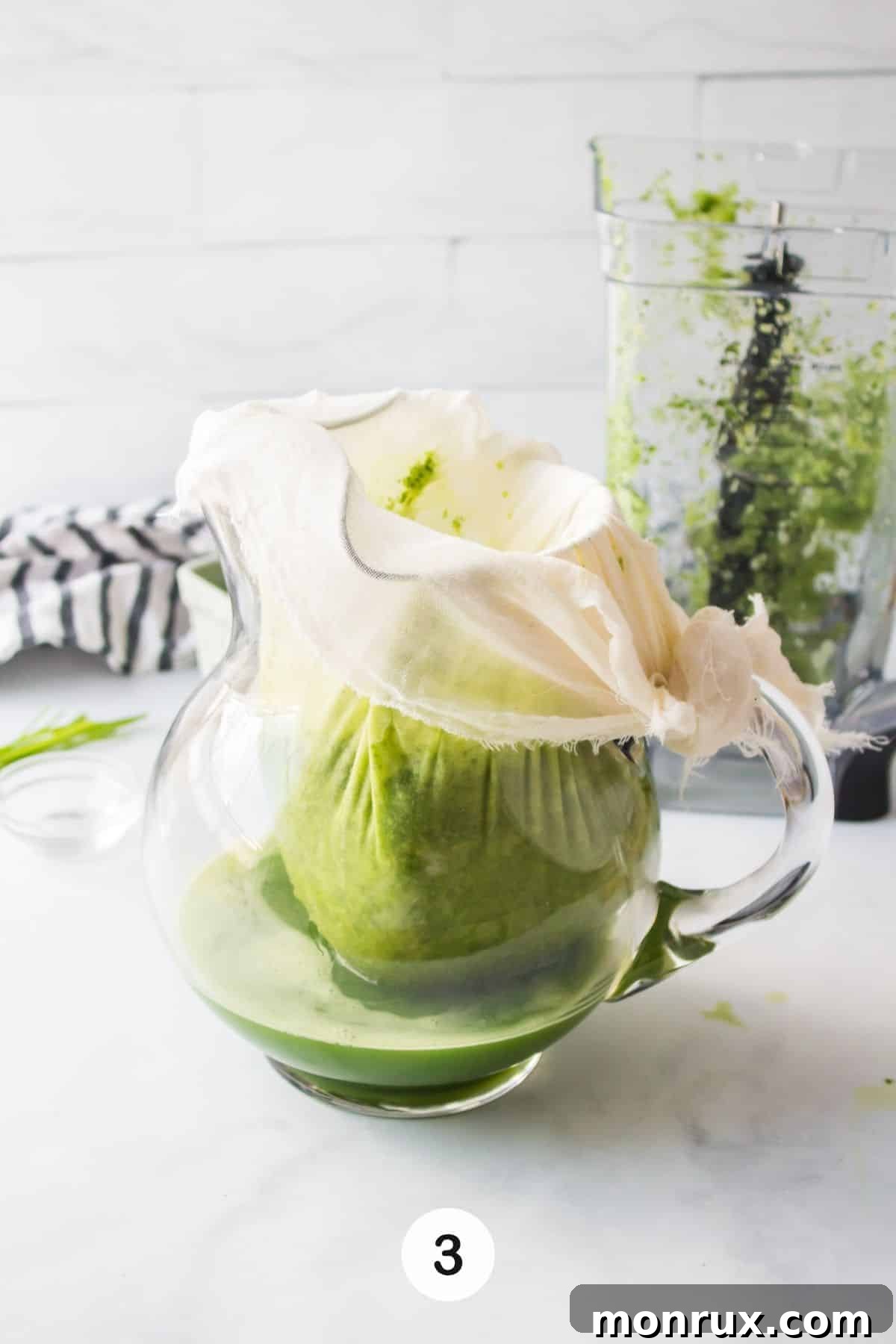 Freshly blended green juice is being carefully strained through a cheesecloth, separating the smooth liquid from the pulp.