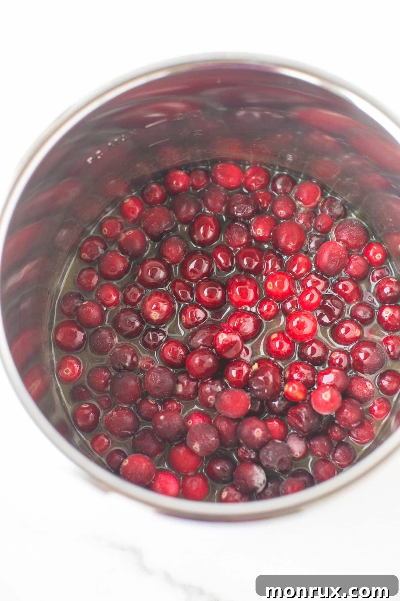 Ingredients for Instant Pot Cranberry Sauce, including frozen cranberries, orange juice, and maple syrup, placed directly into the Instant Pot insert before cooking.