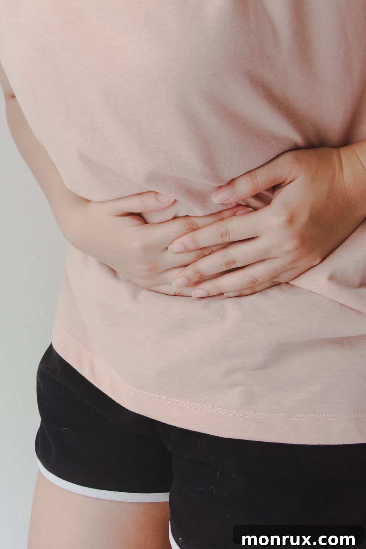 A young woman gently holding her stomach, conveying discomfort and pain, often associated with digestive upset.