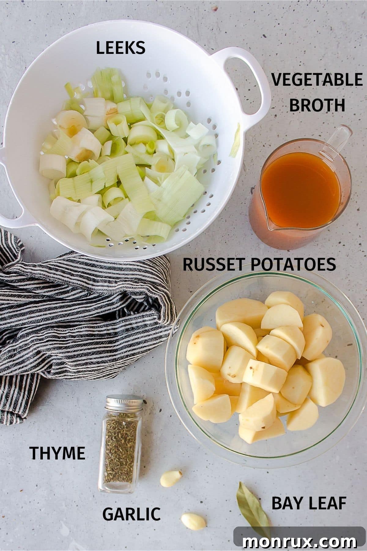Arrangement of fresh ingredients for vegan potato leek soup including leeks, potatoes, garlic, and herbs.