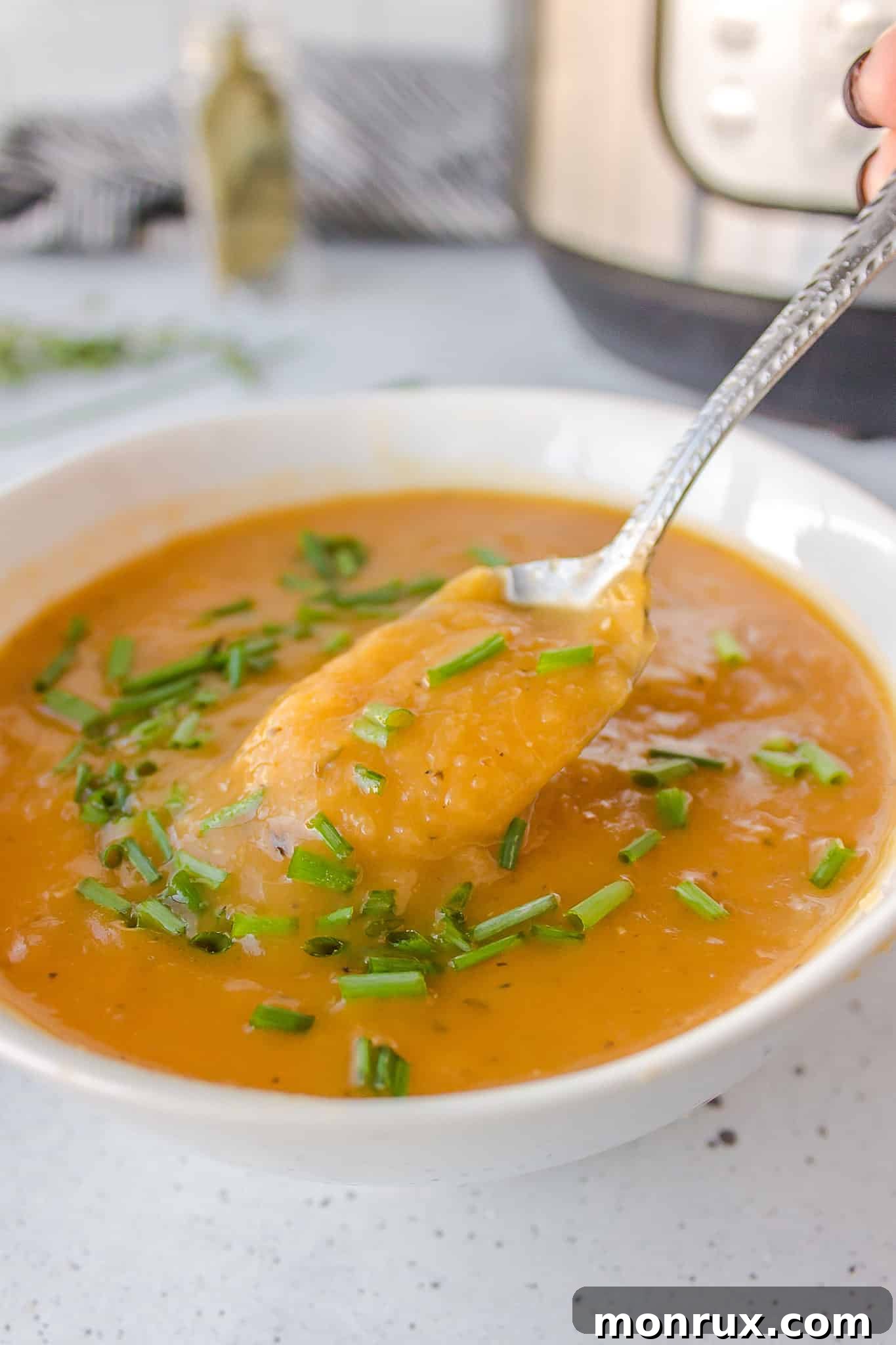 A close-up of a spoonful of creamy vegan potato leek soup garnished with fresh chives.