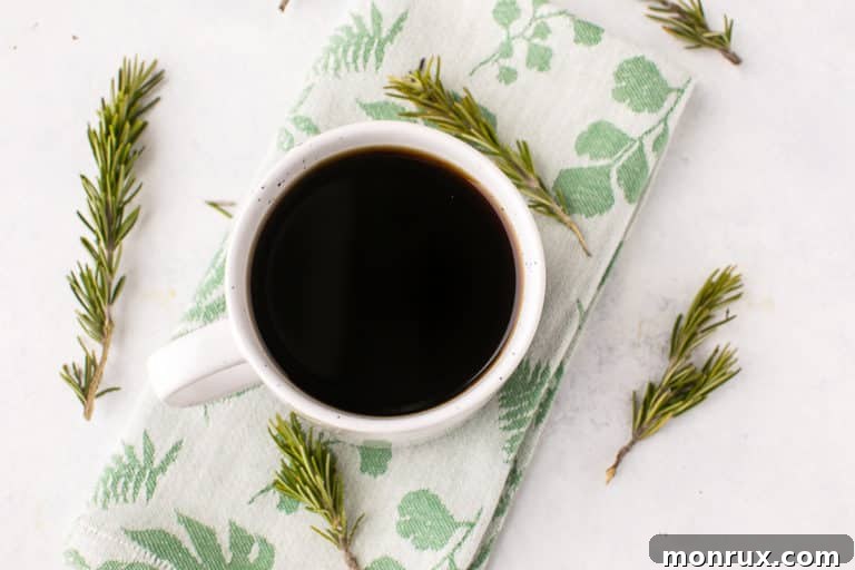 A pristine white mug holds a freshly brewed Rosemary Coffee, enhanced with delicate fresh rosemary sprigs, symbolizing natural wellness and morning invigoration.