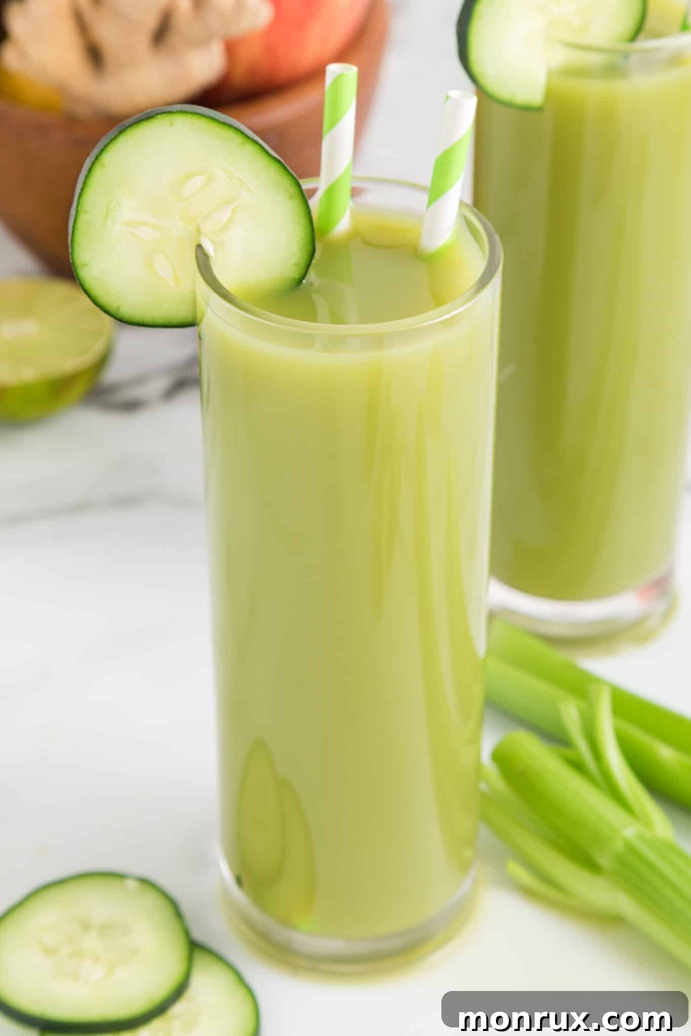 Two glasses of cucumber celery juice with cucumber wheels and straws, ready to be enjoyed.