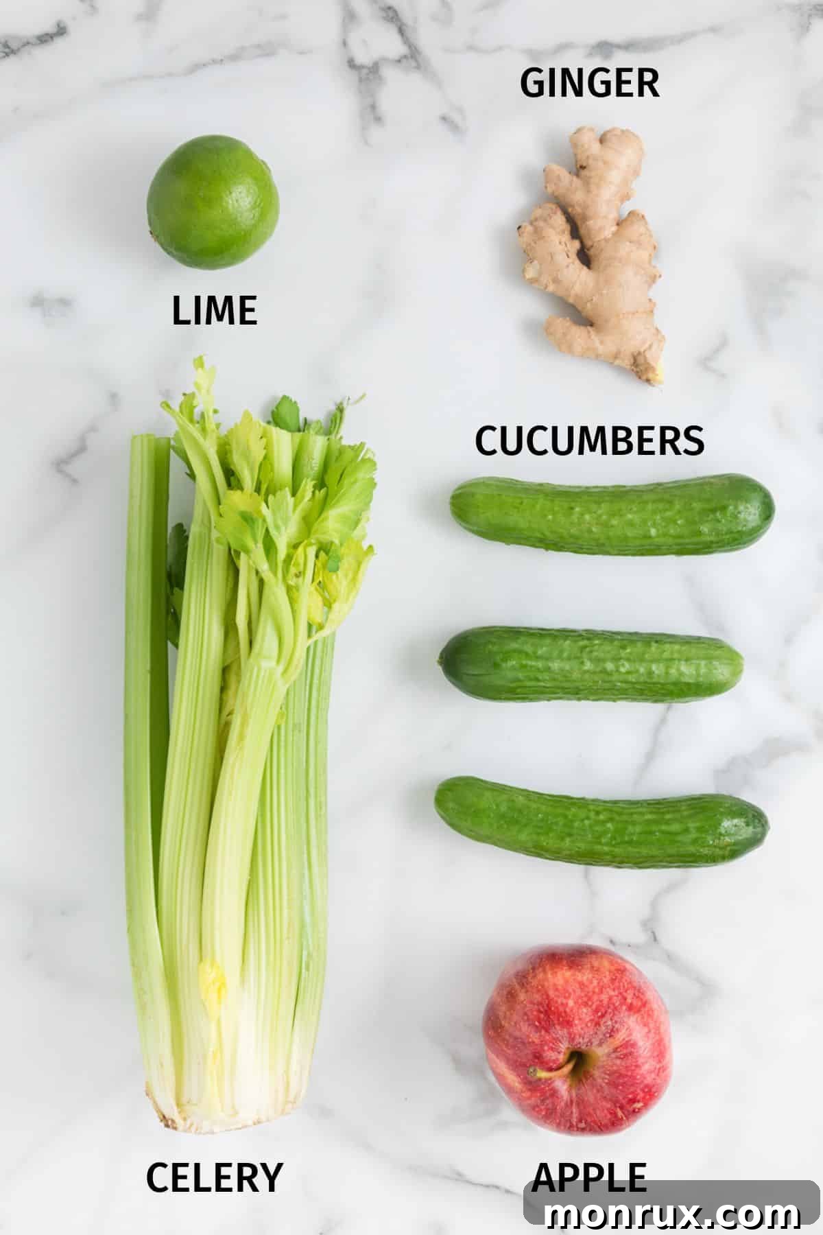 Fresh ingredients laid out on a white surface, including celery, cucumbers, an apple, ginger, and lime, ready for juicing.