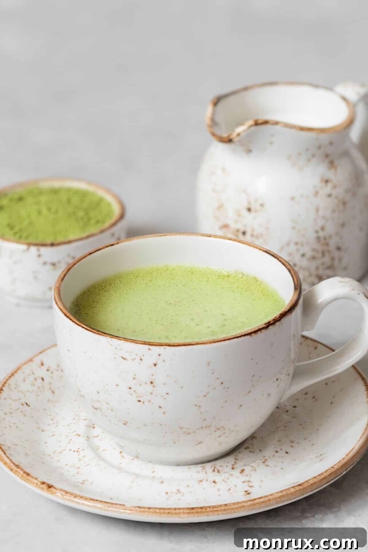 A beautifully presented coconut matcha latte in a ceramic mug, with a small dish of coconut butter on the side.