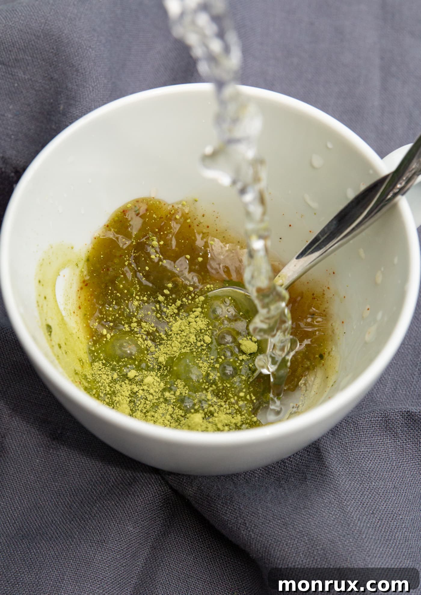 A close-up shot of hot water being poured into a mug containing matcha powder, coconut butter, and coconut sugar.