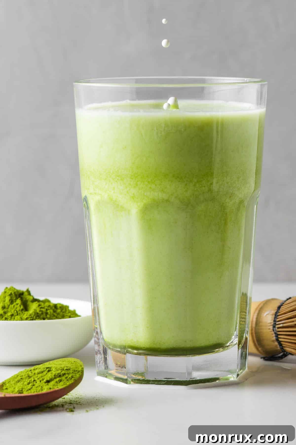 An iced coconut matcha latte in a clear glass, garnished with a straw.