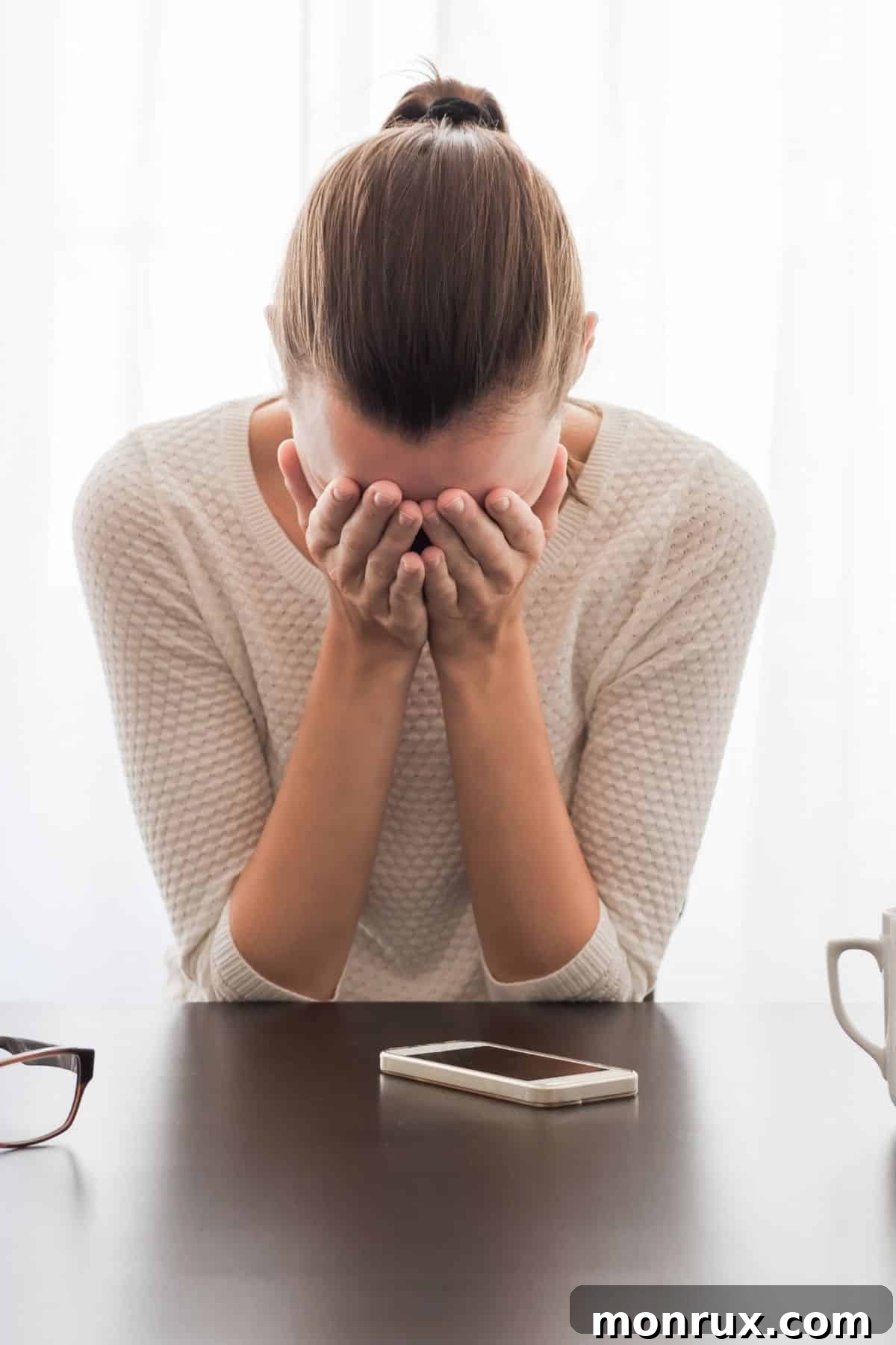 Woman sitting at a table, holding her head in her hands, looking exhausted.