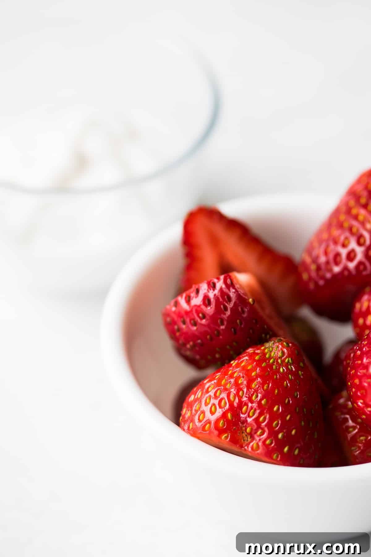 Bowl of fresh strawberries next to a container of coconut yogurt, ready for blending.
