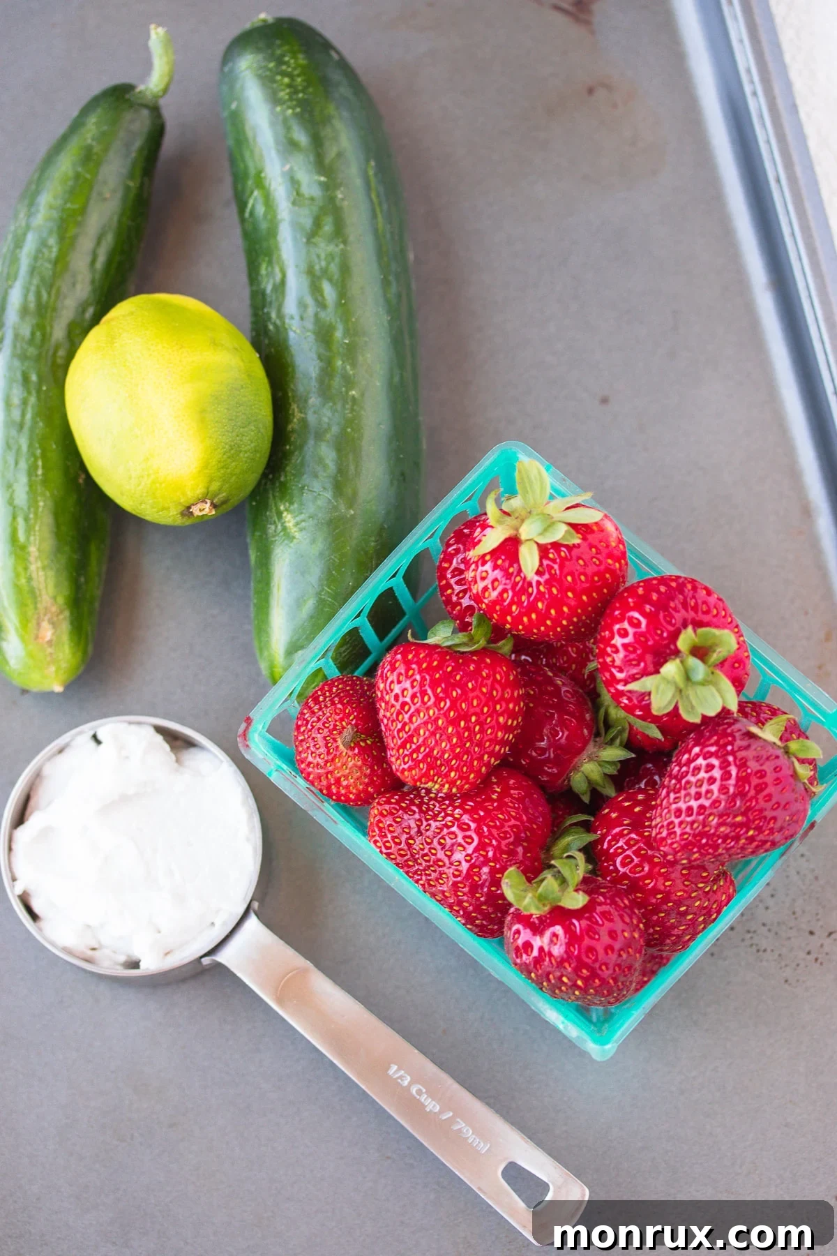 A vibrant flat lay of the fresh ingredients for cold strawberry bisque soup, including ripe strawberries, a green cucumber, a lime, and a can of coconut cream.