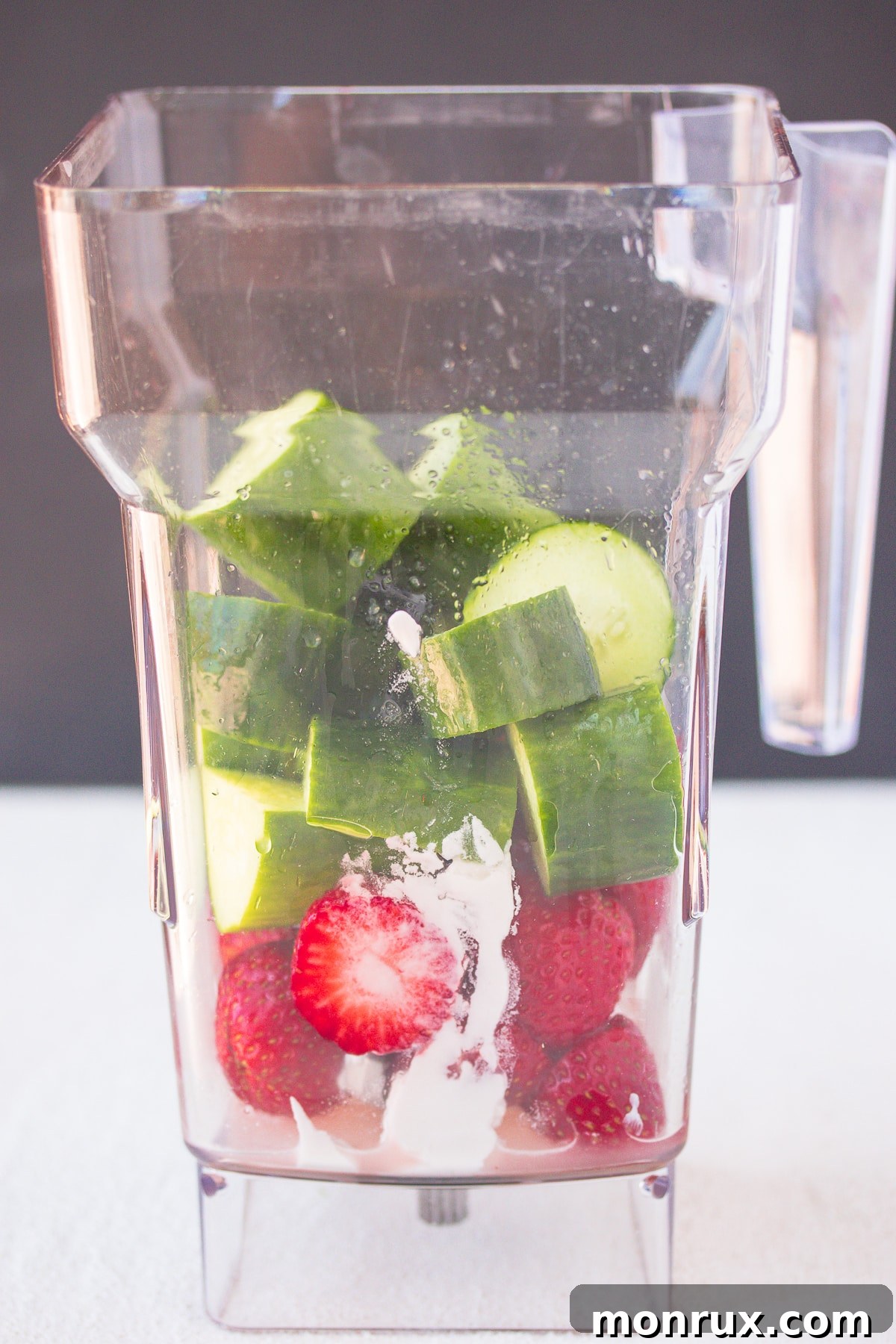 Close-up shot of fresh strawberries, cucumber slices, and coconut cream being added to the base of a high-speed blender, ready to be processed into soup.