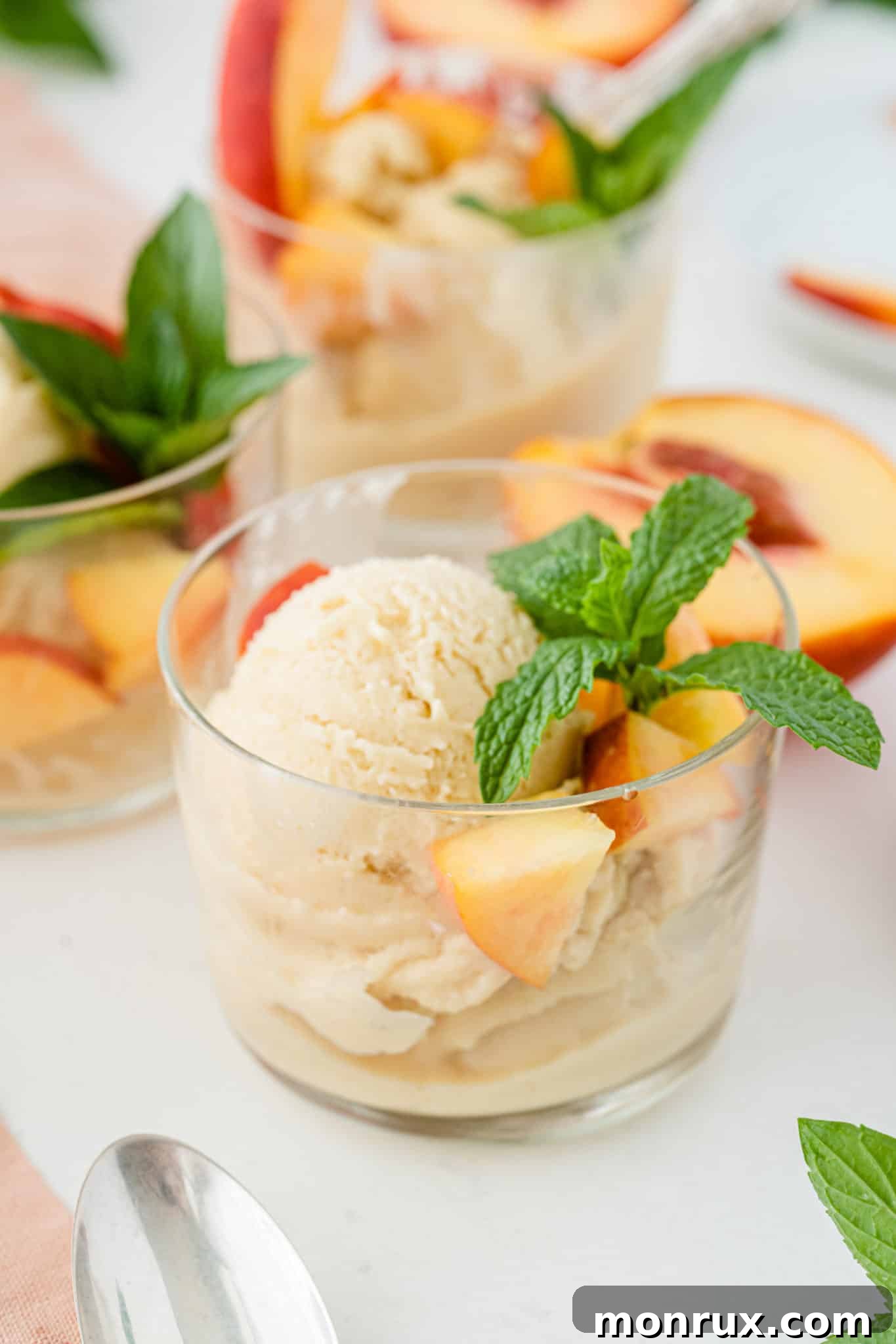 A bowl of creamy vegan peach ice cream, garnished with fresh mint leaves, perfect for a summer treat.