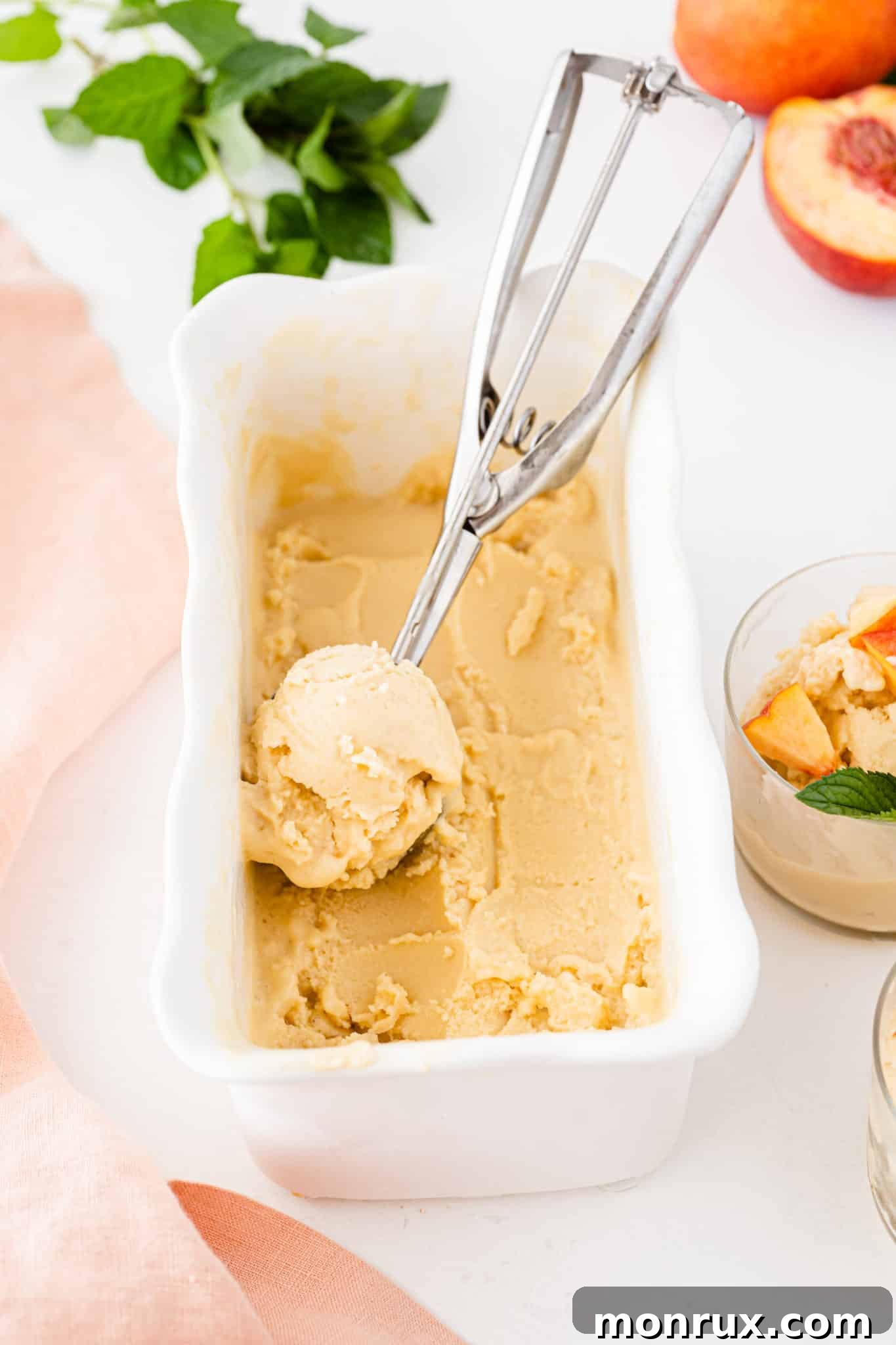 A container of creamy vegan peach ice cream with a scoop ready to serve.