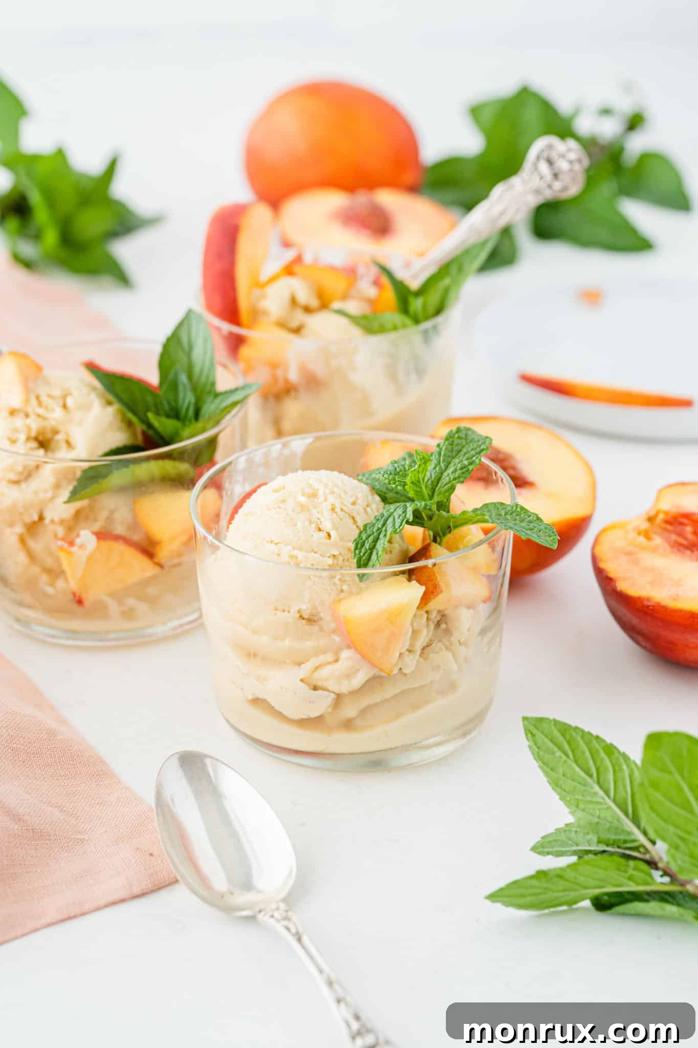 Two bowls of homemade peach ice cream, garnished with fresh mint, sitting on a rustic wooden table with spoons beside them.