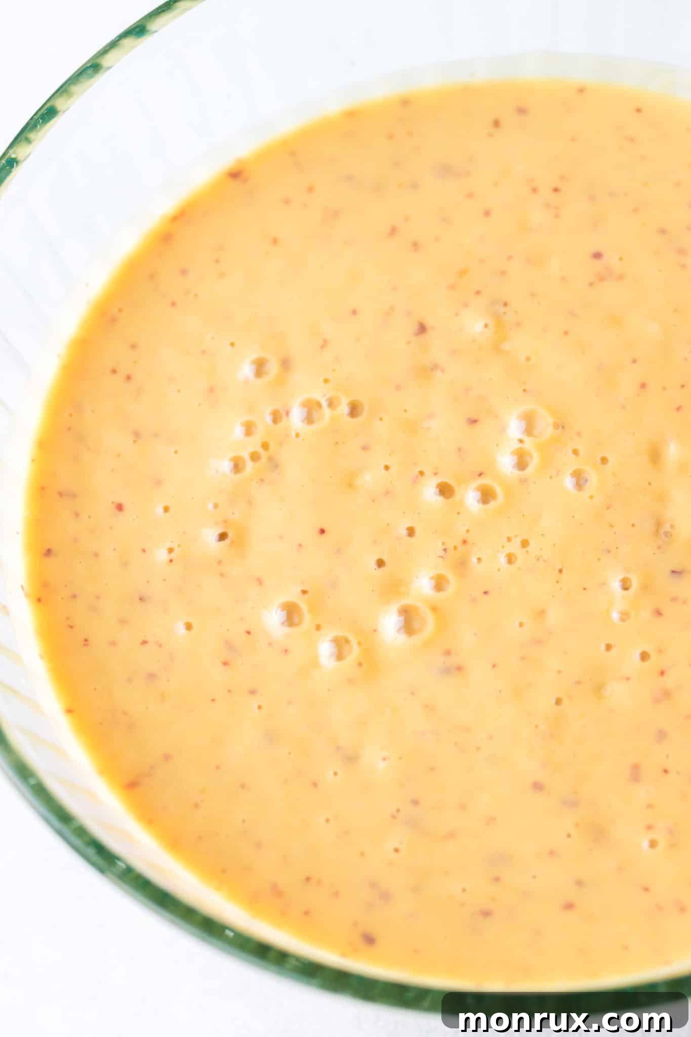 A creamy, light-colored ice cream mixture in a clear glass bowl, ready for freezing.