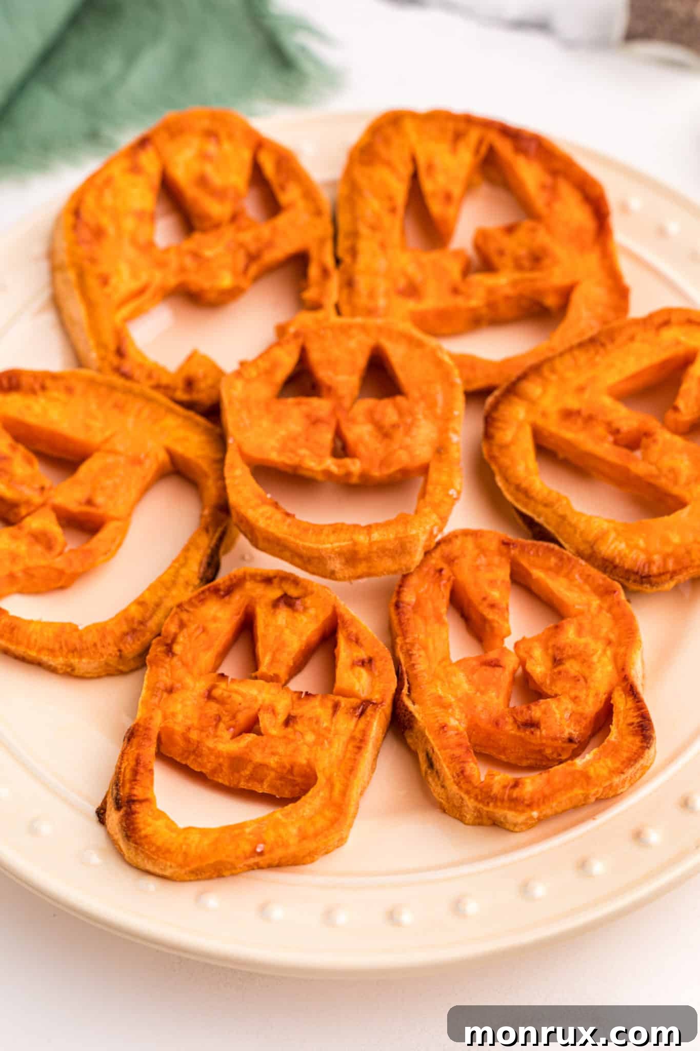 Festive sweet potato slices carved into jack-o'-lantern faces and arranged on a plate.