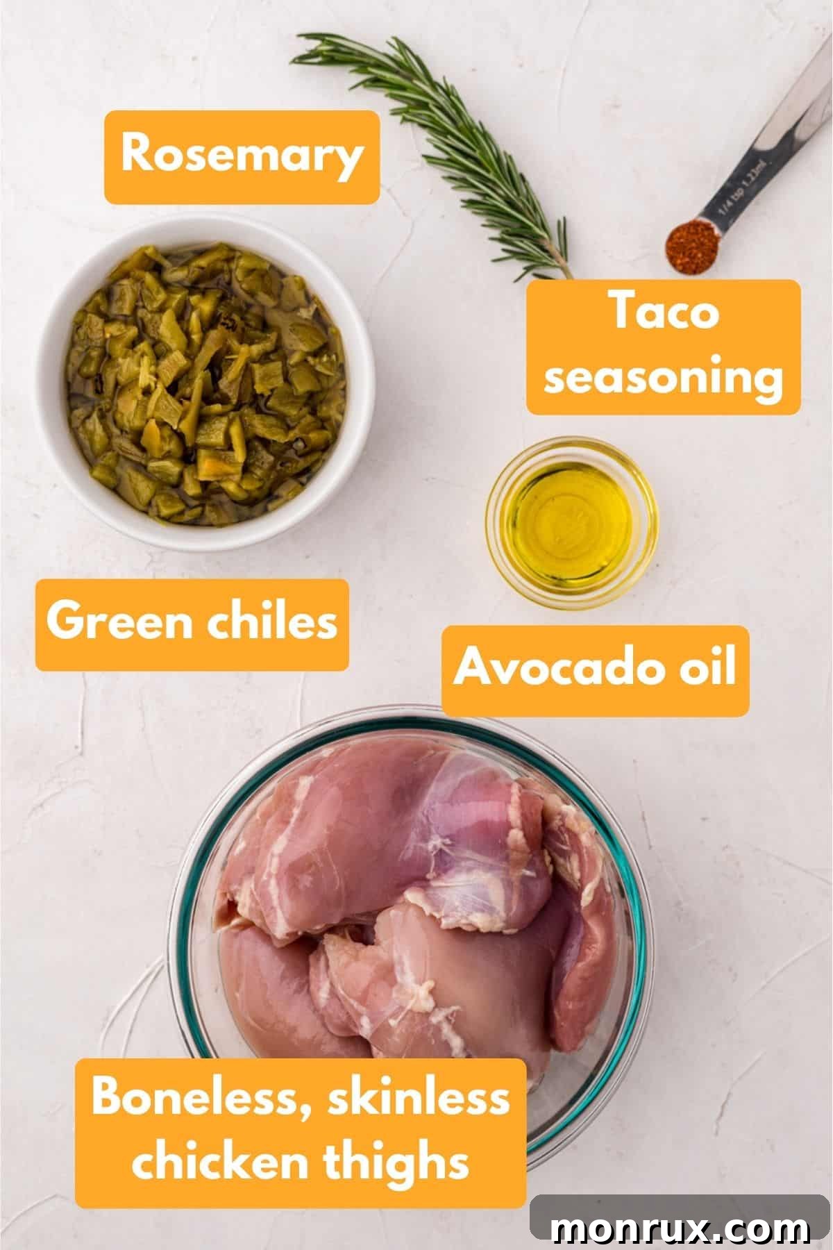 A flat lay photograph showcasing the five simple ingredients for Slow Cooker Green Chile Chicken: raw chicken thighs, a sprig of fresh rosemary, taco seasoning, and cans of diced green chiles.