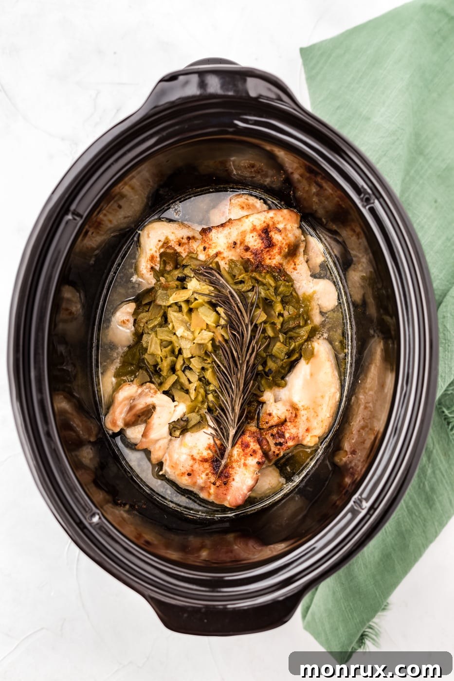 A close-up shot of a slow cooker filled with tender green chile chicken, ready to be served.