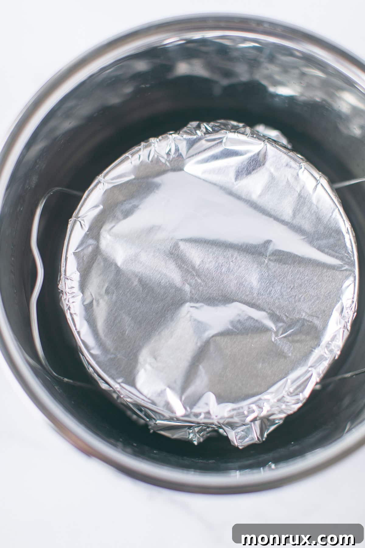 A perfectly wrapped cake pan, sealed with aluminum foil, carefully positioned on the trivet inside the Instant Pot pressure cooker, ready for cooking.