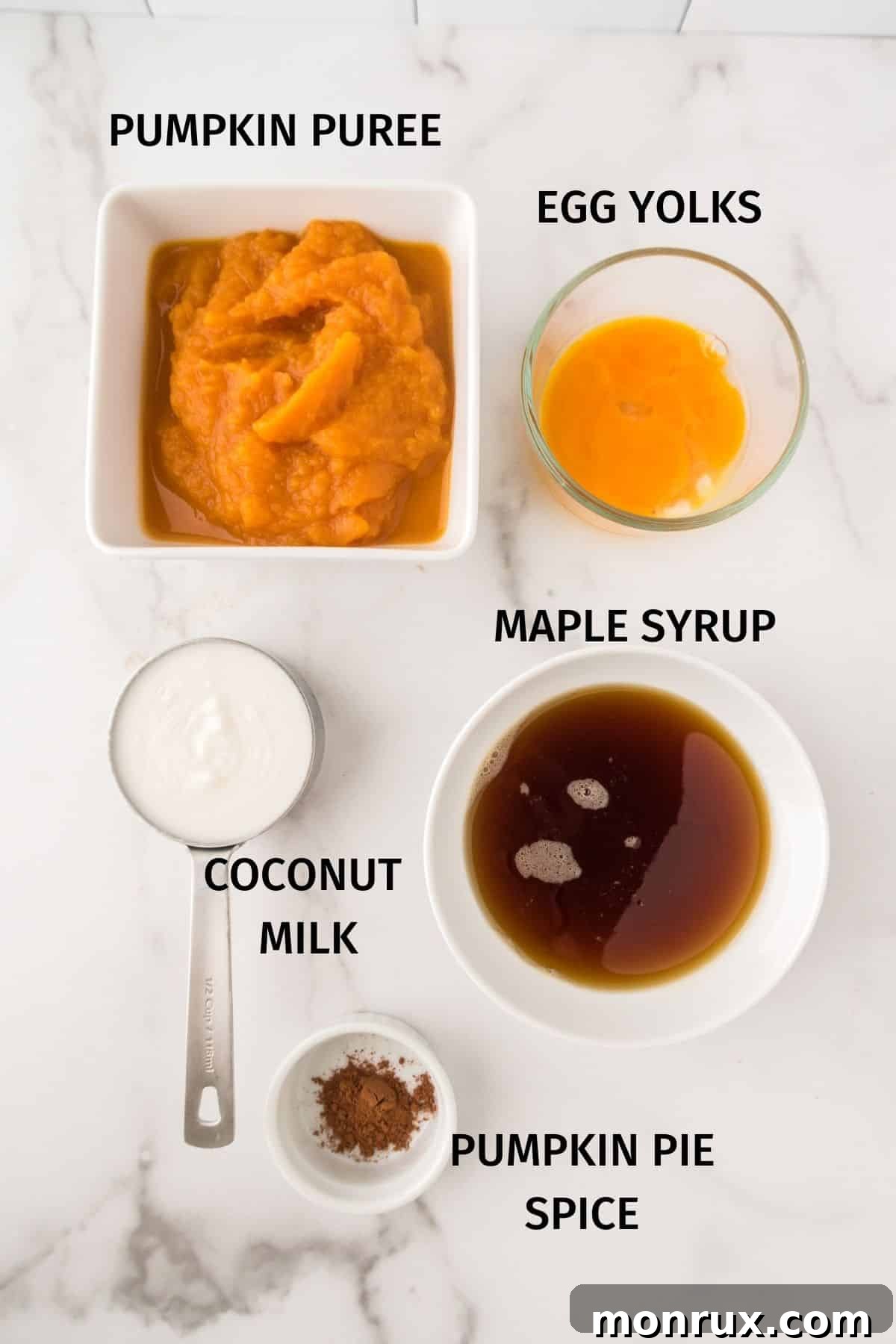 A selection of fresh ingredients laid out on a kitchen counter for Instant Pot pumpkin pudding, including a can of pumpkin puree, eggs, a bottle of maple syrup, a can of coconut milk, and pumpkin pie spice.