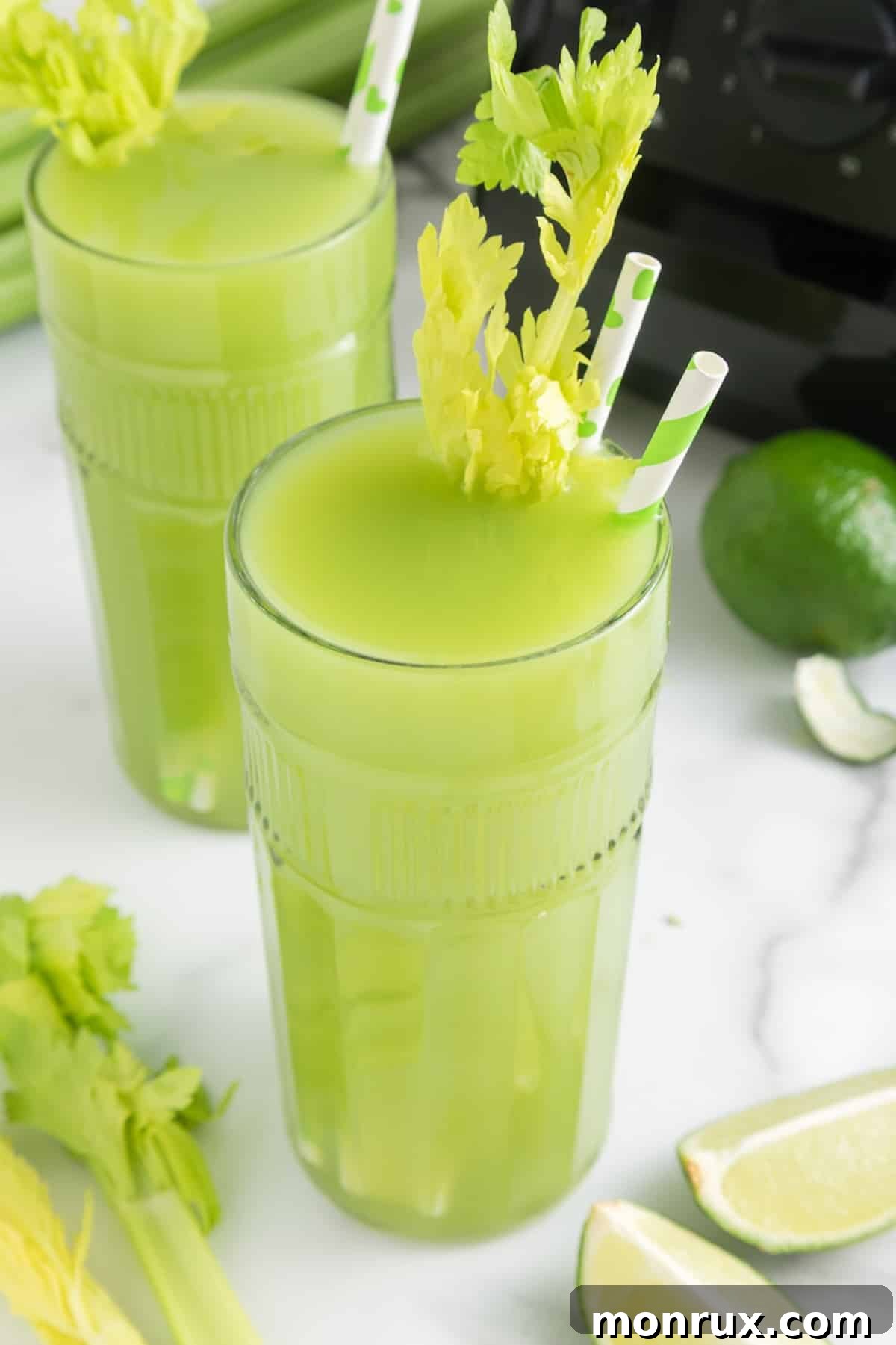 Two glasses of vibrant green celery juice with striped straws, ready to be enjoyed.