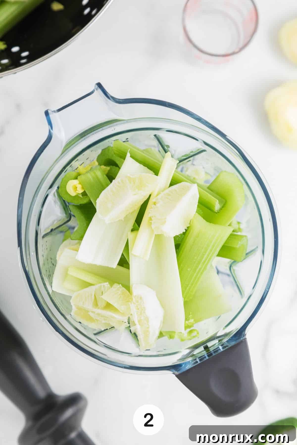 Chopped celery stalks and a peeled lime placed inside a blender, ready for blending.
