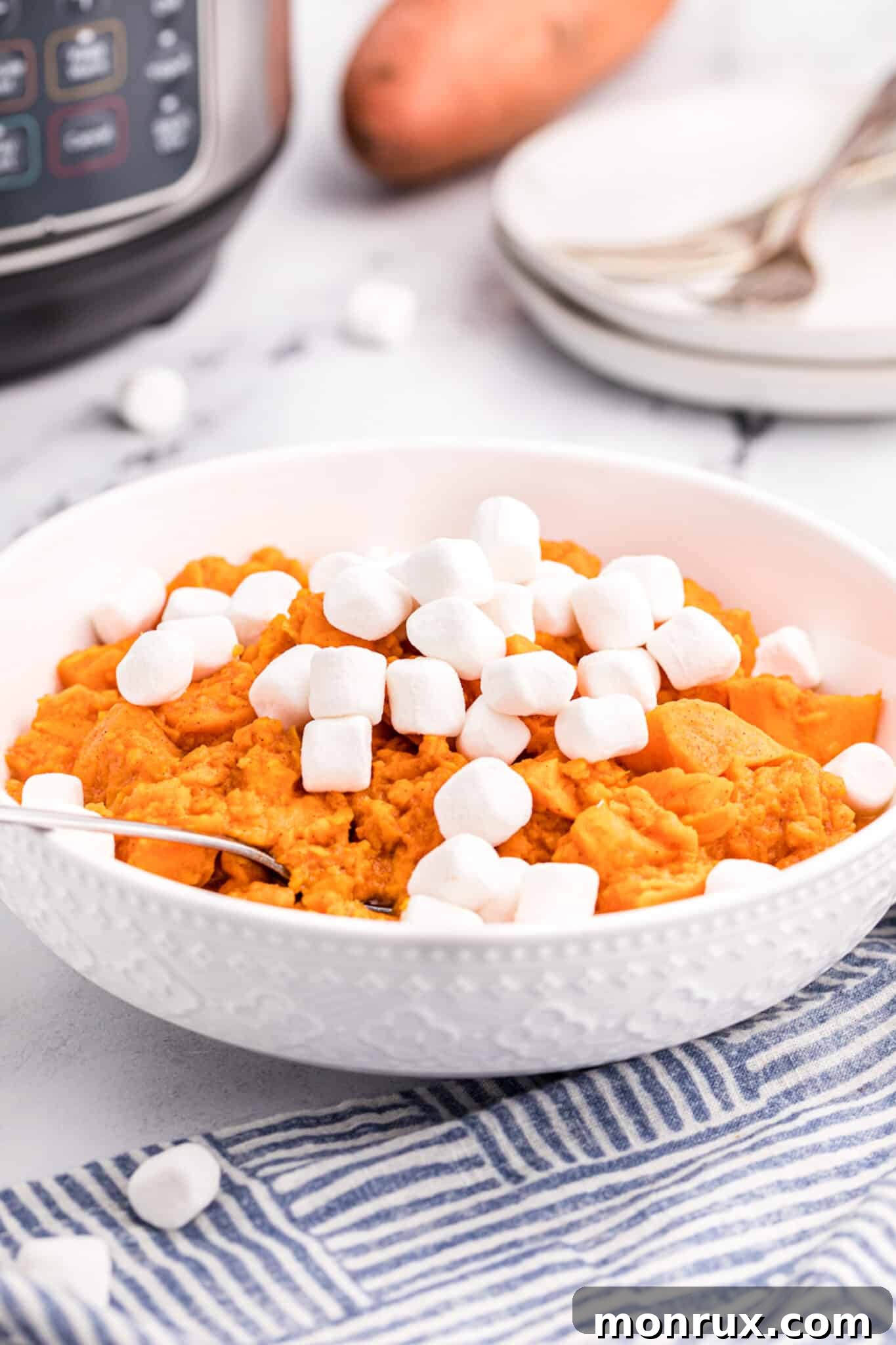 A white serving bowl with glistening candied yams topped with perfectly toasted mini marshmallows, ready for a festive table.