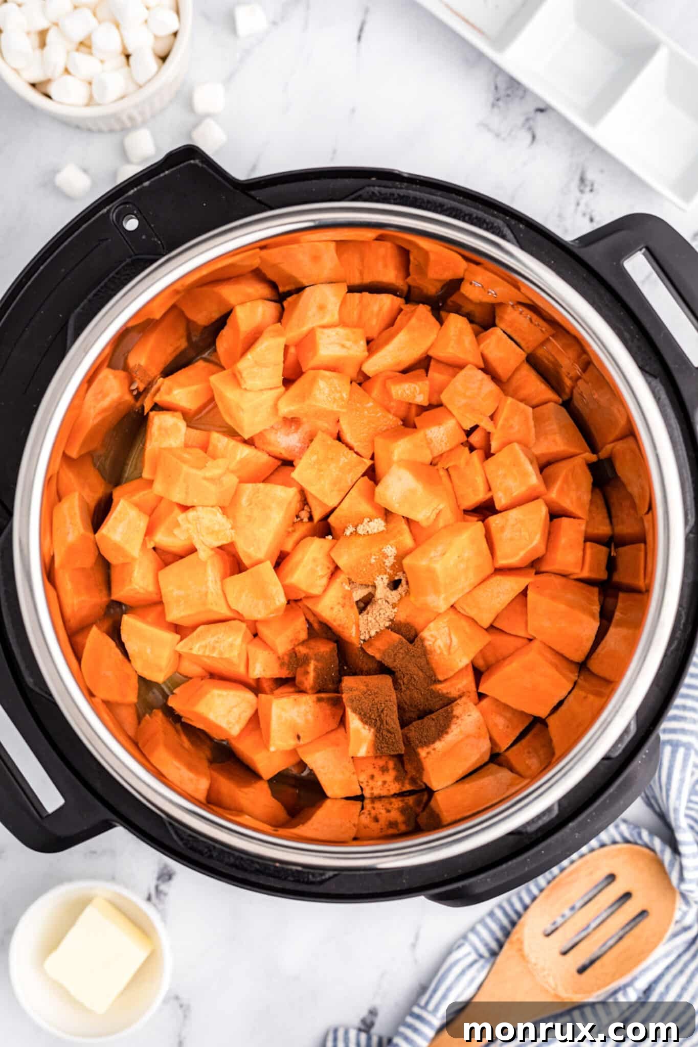 Peeled and chopped yams inside an Instant Pot, mixed with orange juice and maple syrup.