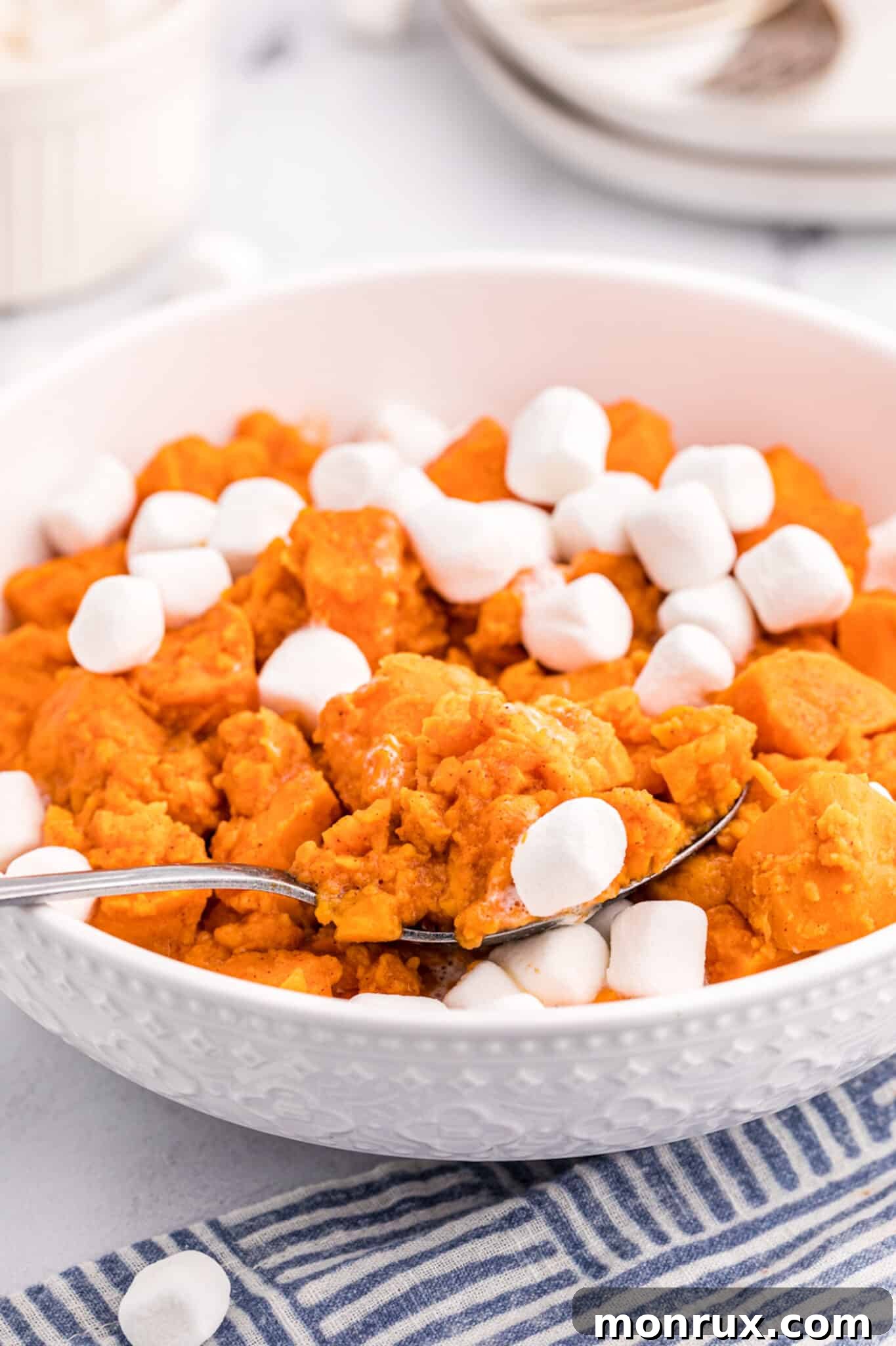 A white serving bowl with glistening candied yams topped with perfectly toasted mini marshmallows, ready for a festive table.
