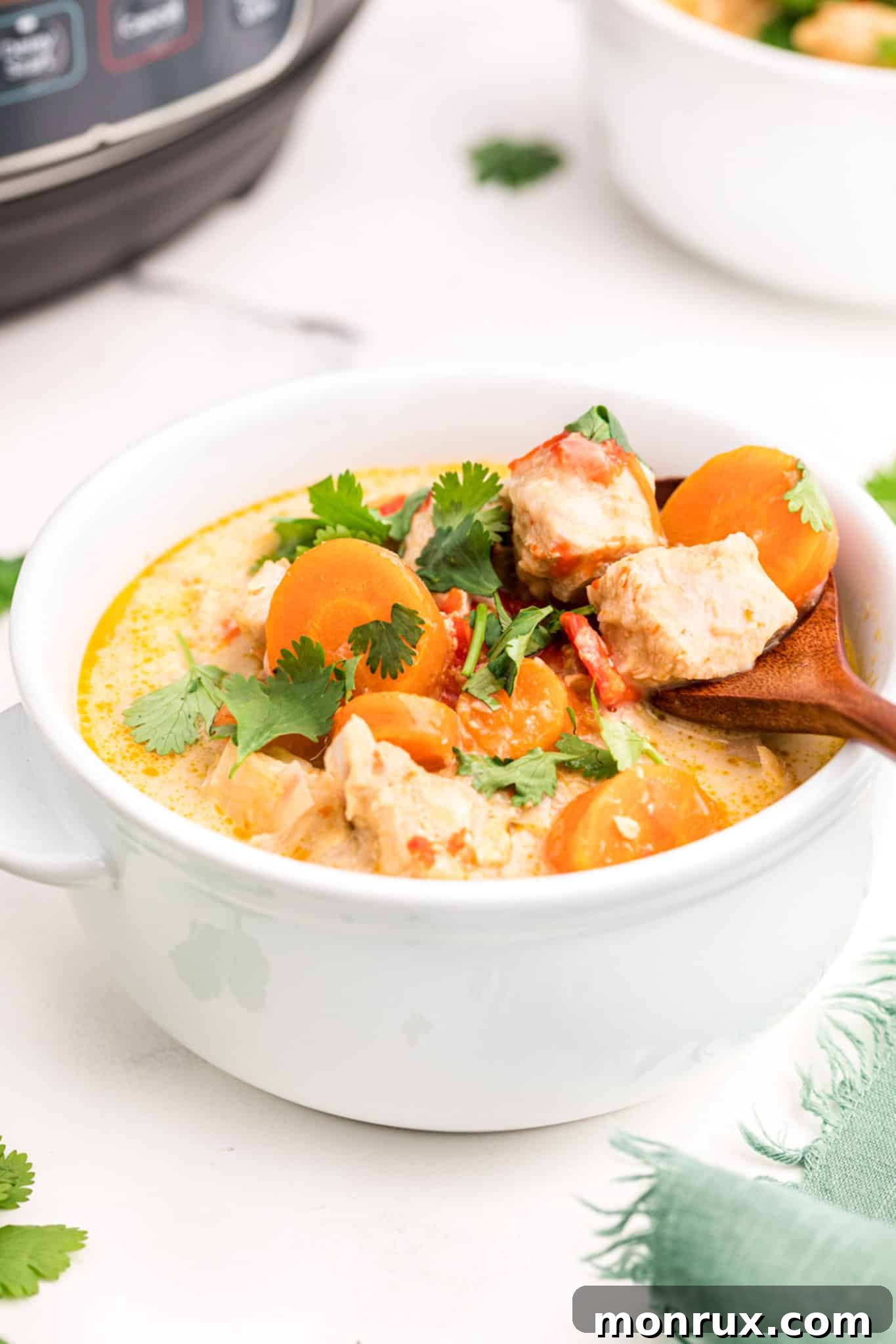 A wooden spoon in a small white bowl of creamy Instant Pot Thai Chicken Curry Soup, garnished with fresh cilantro.