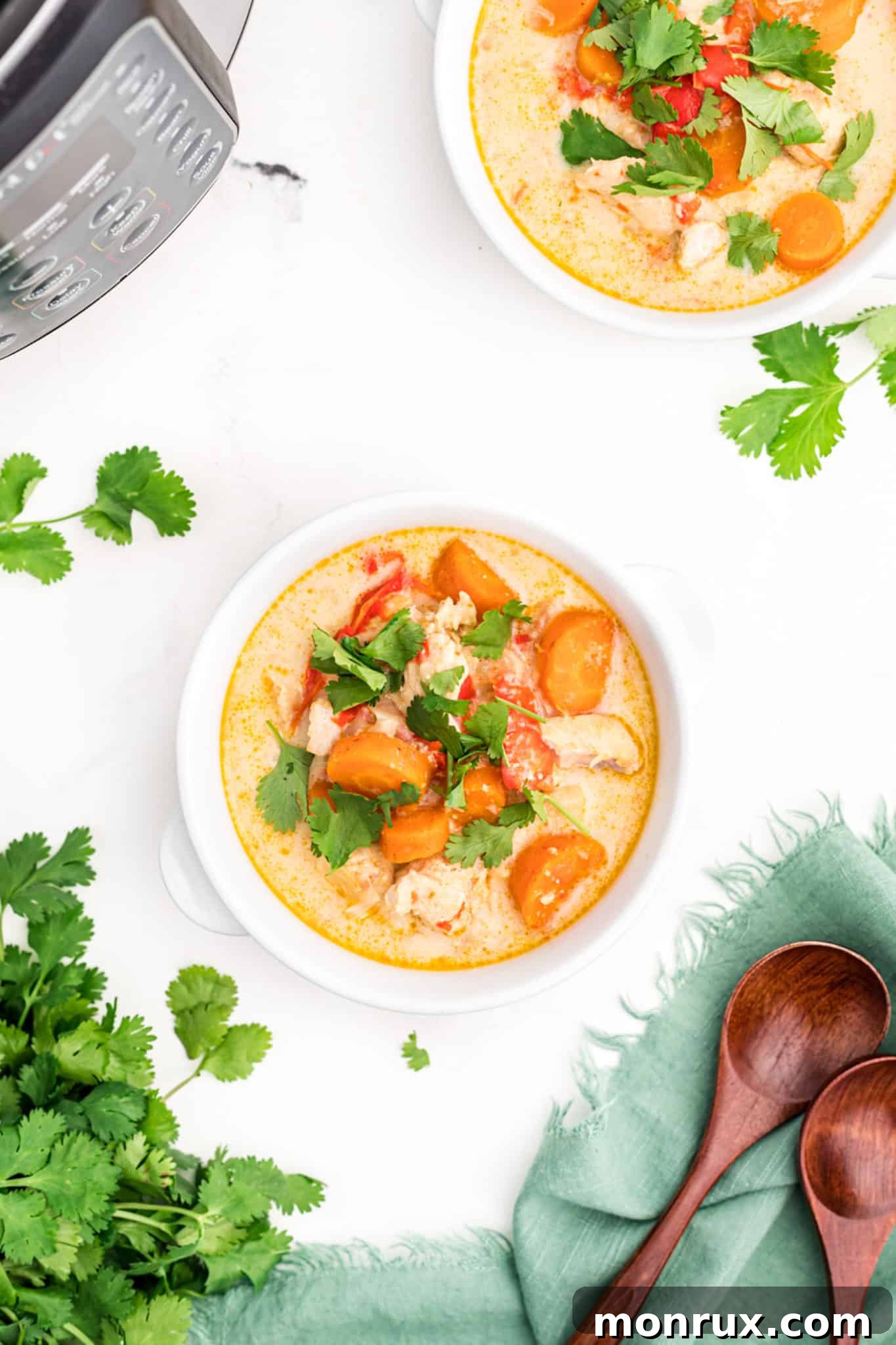 Top-down view of a small white bowl of Instant Pot Thai Chicken Curry Soup, with visible chicken, vegetables, and cilantro garnish.