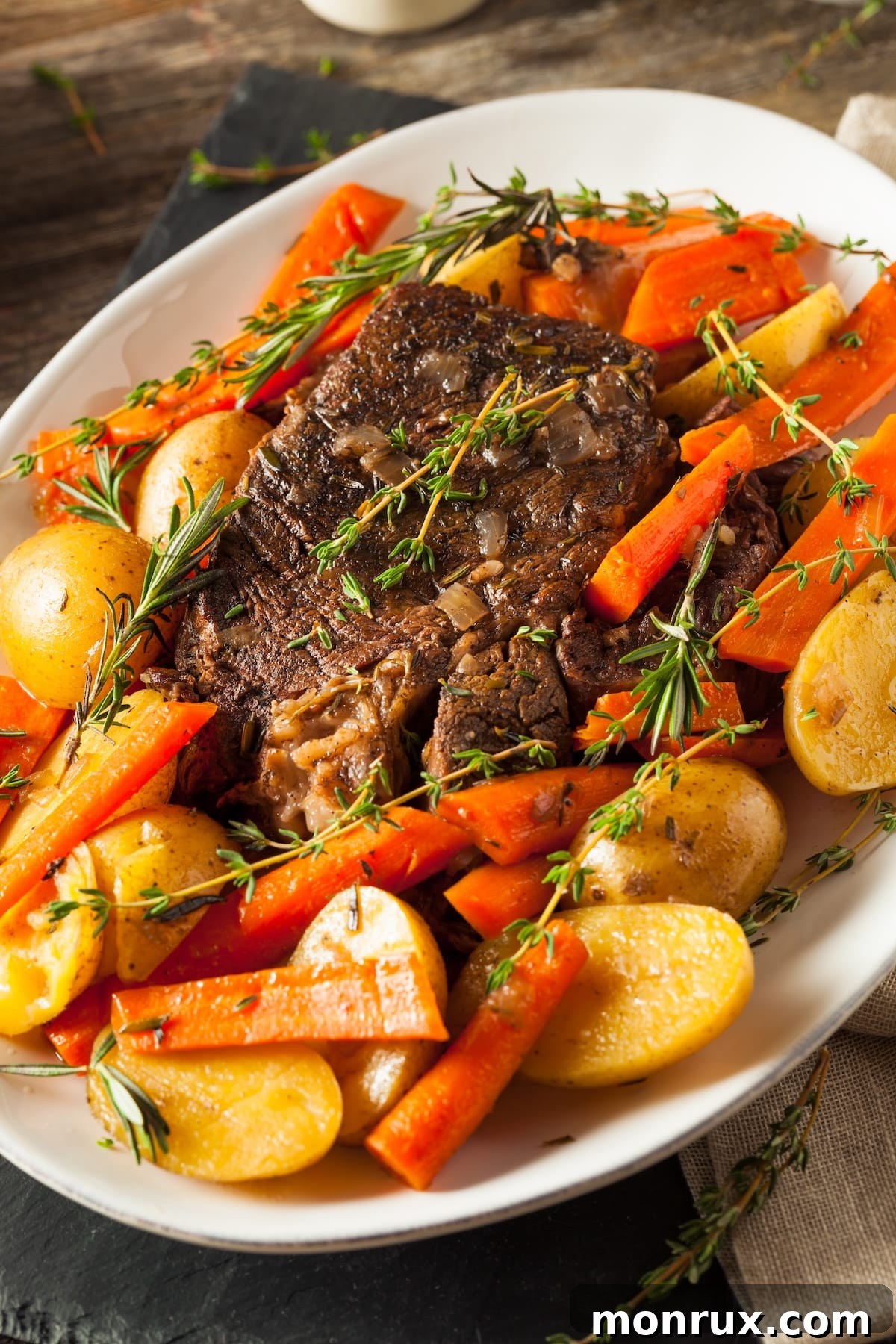 A beautifully cooked tri tip crockpot roast on a serving platter surrounded by colorful, tender vegetables.