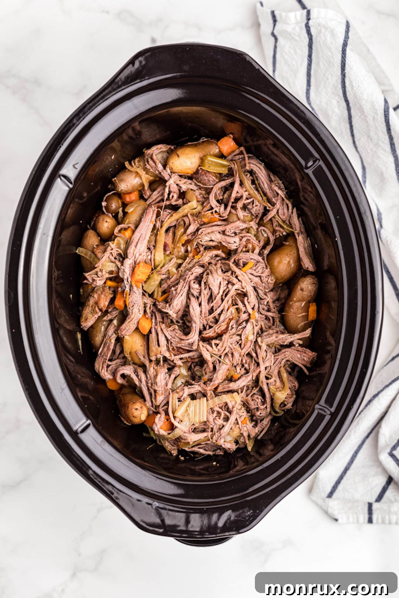 Shredded tri tip roast with tender vegetables mixed together in a slow cooker, ready to be served.