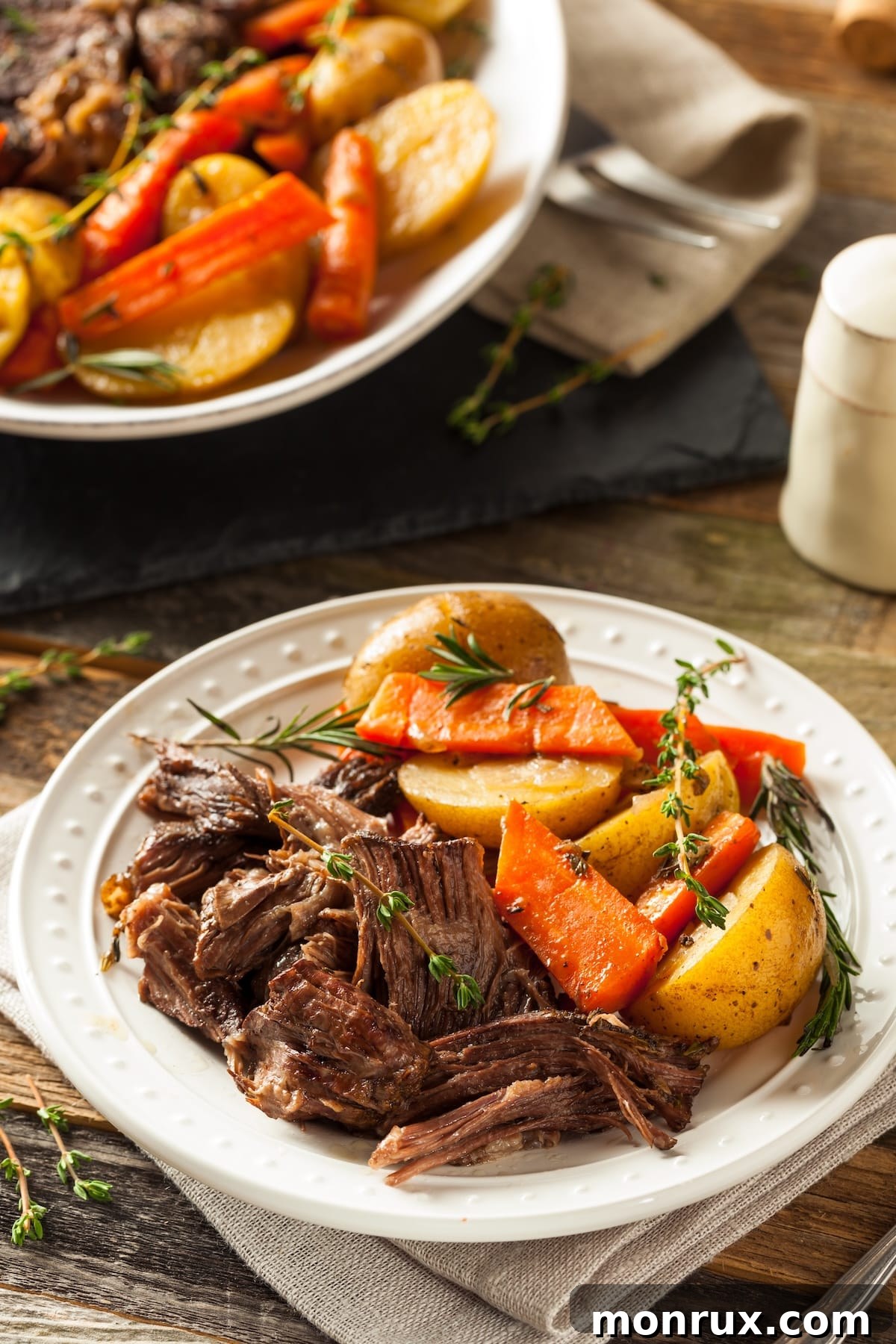 A serving plate filled with slow cooker tri tip roast and mixed vegetables, garnished with fresh herbs.