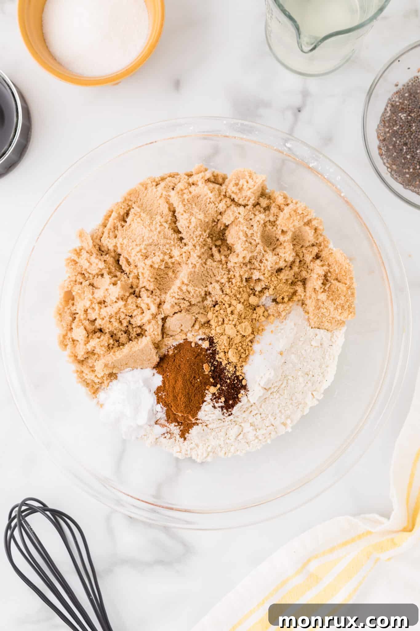 A large mixing bowl filled with dry cookie ingredients, including flour, brown sugar, baking soda, and various spices, ready to be combined.