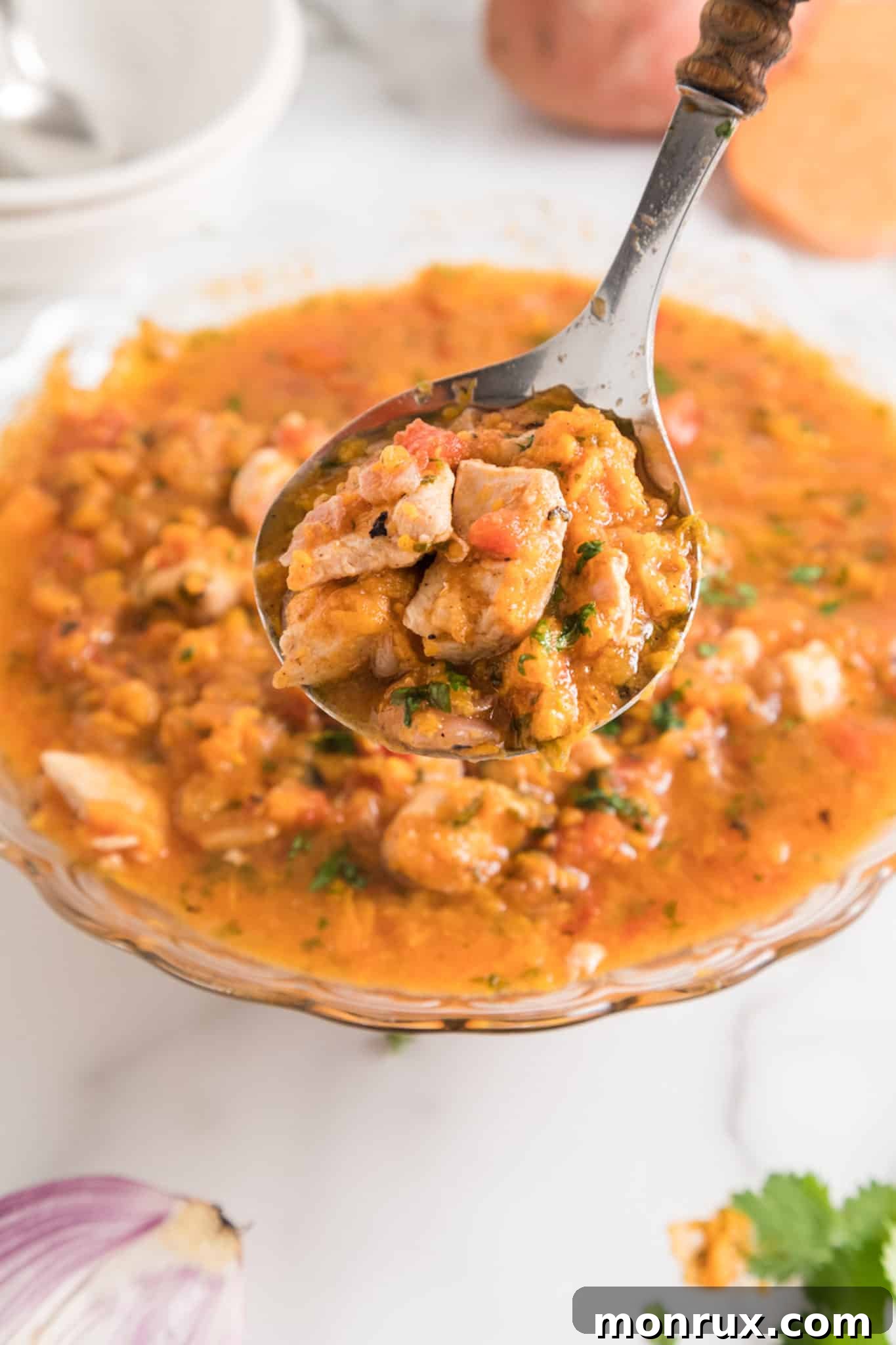 A spoonful of instant pot sweet potato chicken over a serving bowl, showcasing the rich colors and textures.