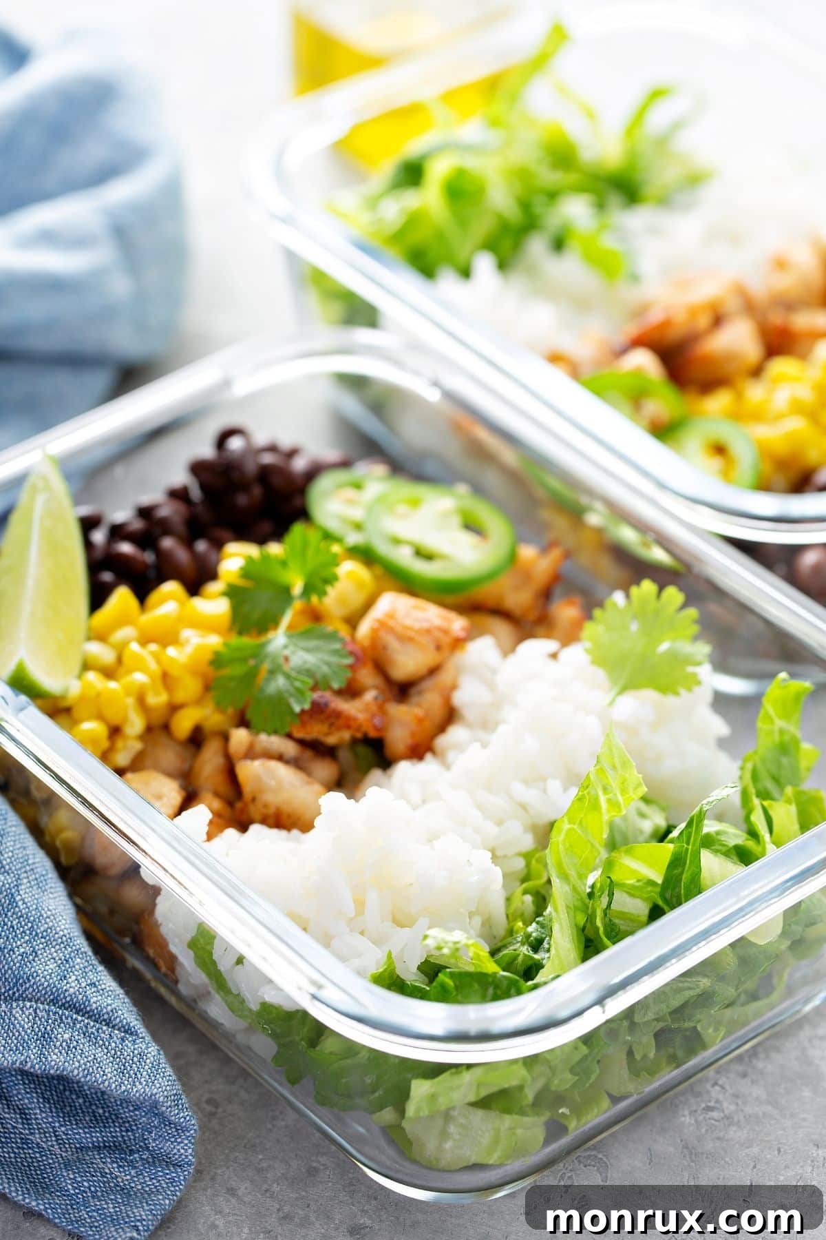 A close-up of a neatly arranged glass meal prep container with chicken, rice, and black beans.
