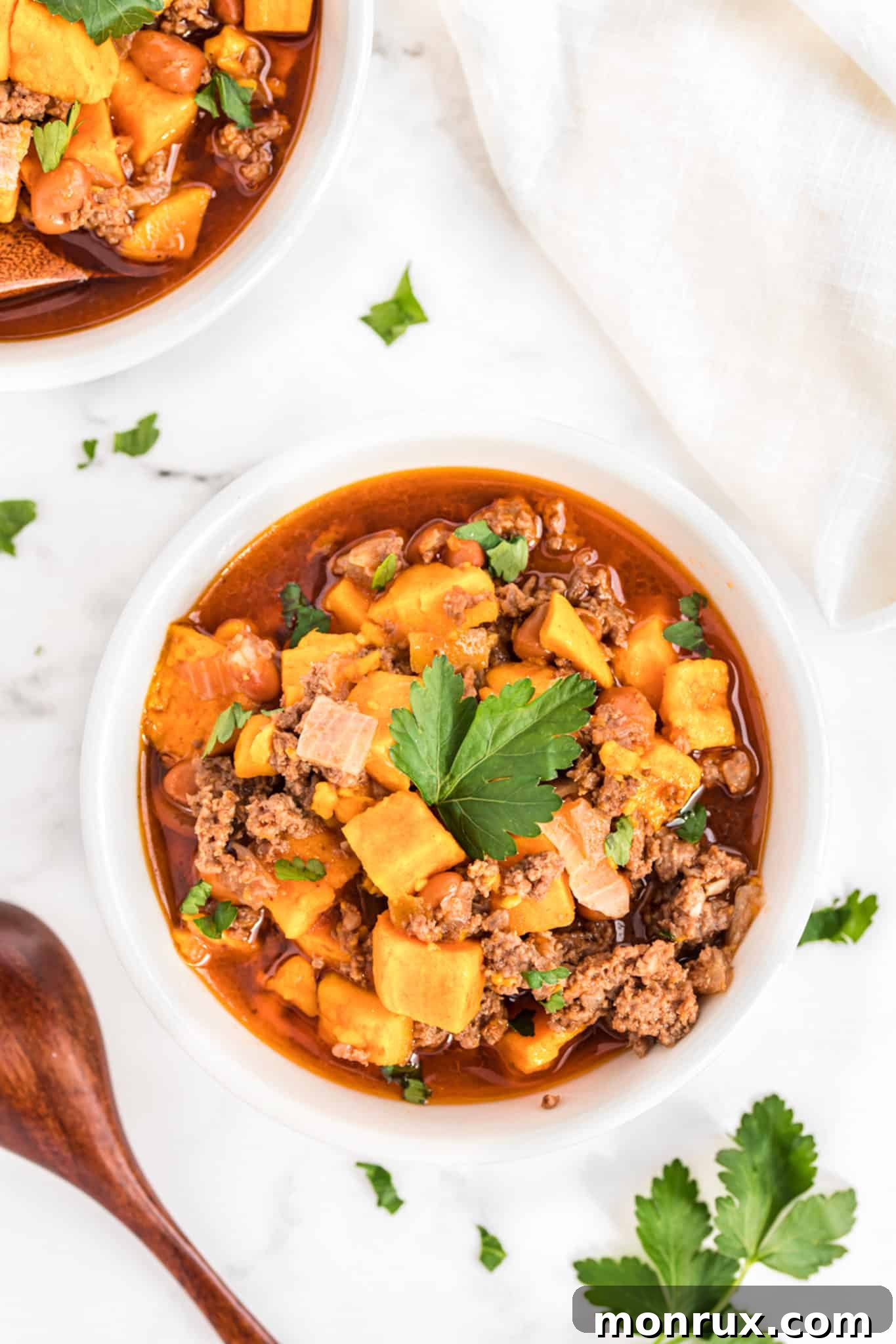 two bowls of sweet potato beef chili with fresh parsley on top.
