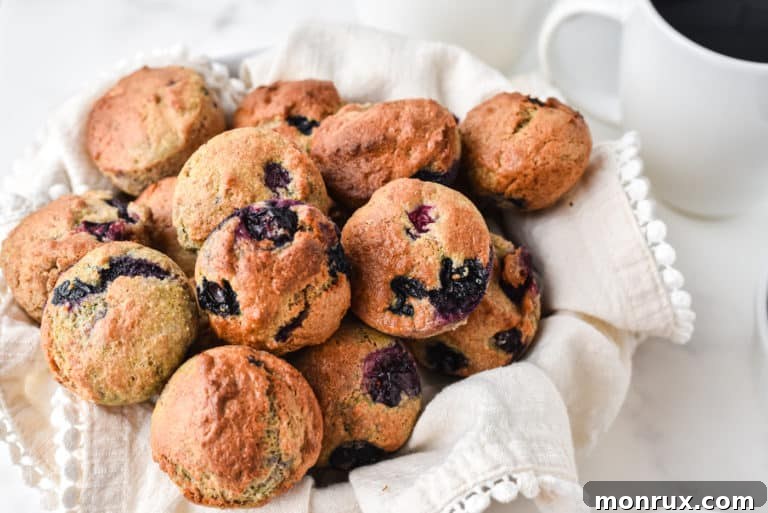 Blueberry mini muffins in a towel-lined basket next to a mug of coffee.