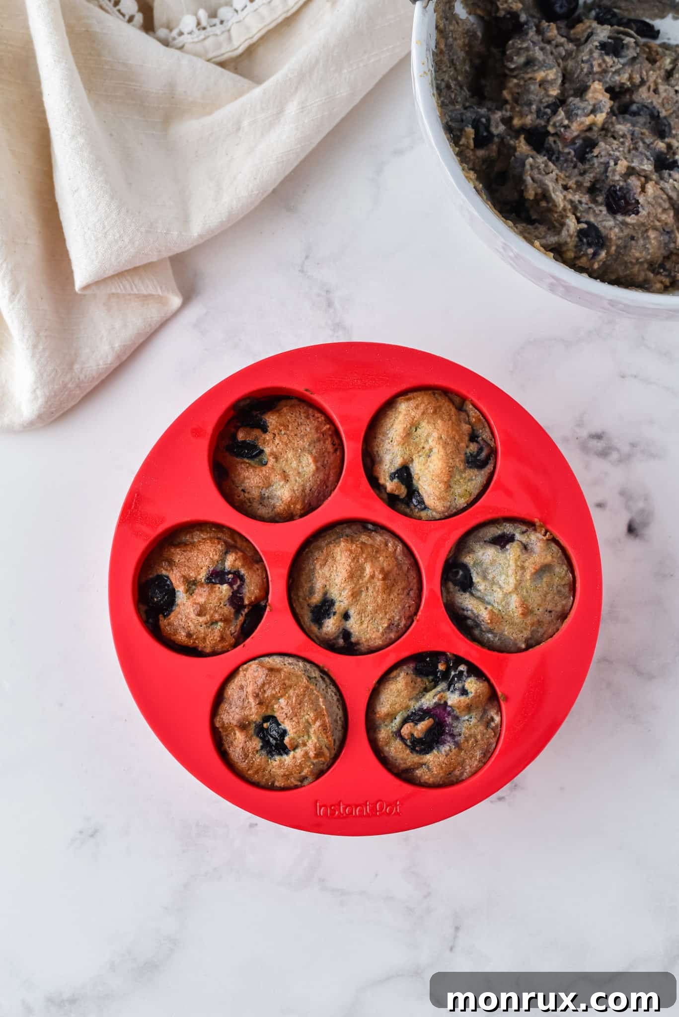 Six perfectly baked mini blueberry muffins resting in a vibrant red silicone muffin mold, showcasing their golden tops and visible blueberries.