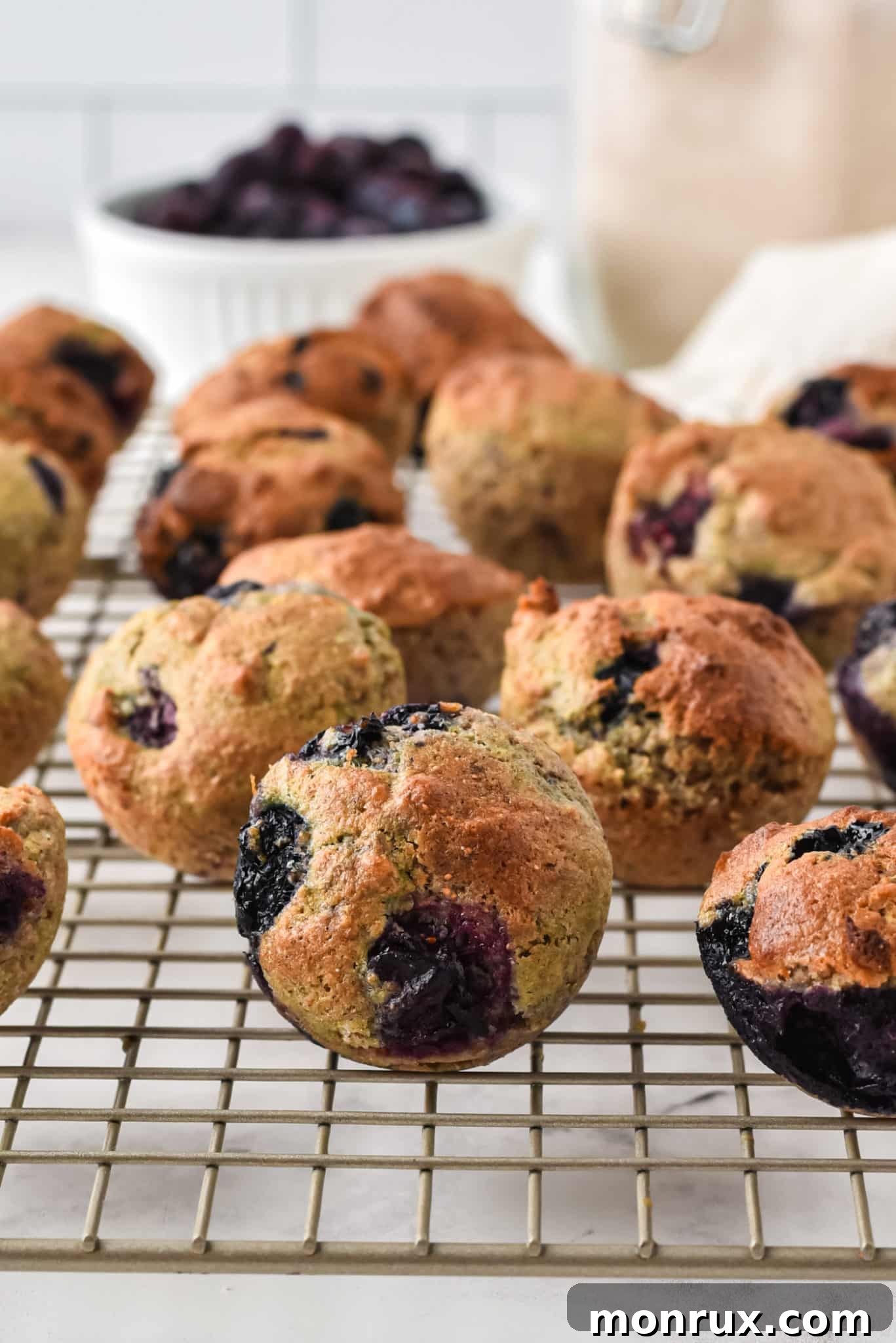 A collection of mini blueberry muffins arranged neatly on a wire cooling rack, highlighting their perfectly baked texture and vibrant blueberry inclusions.