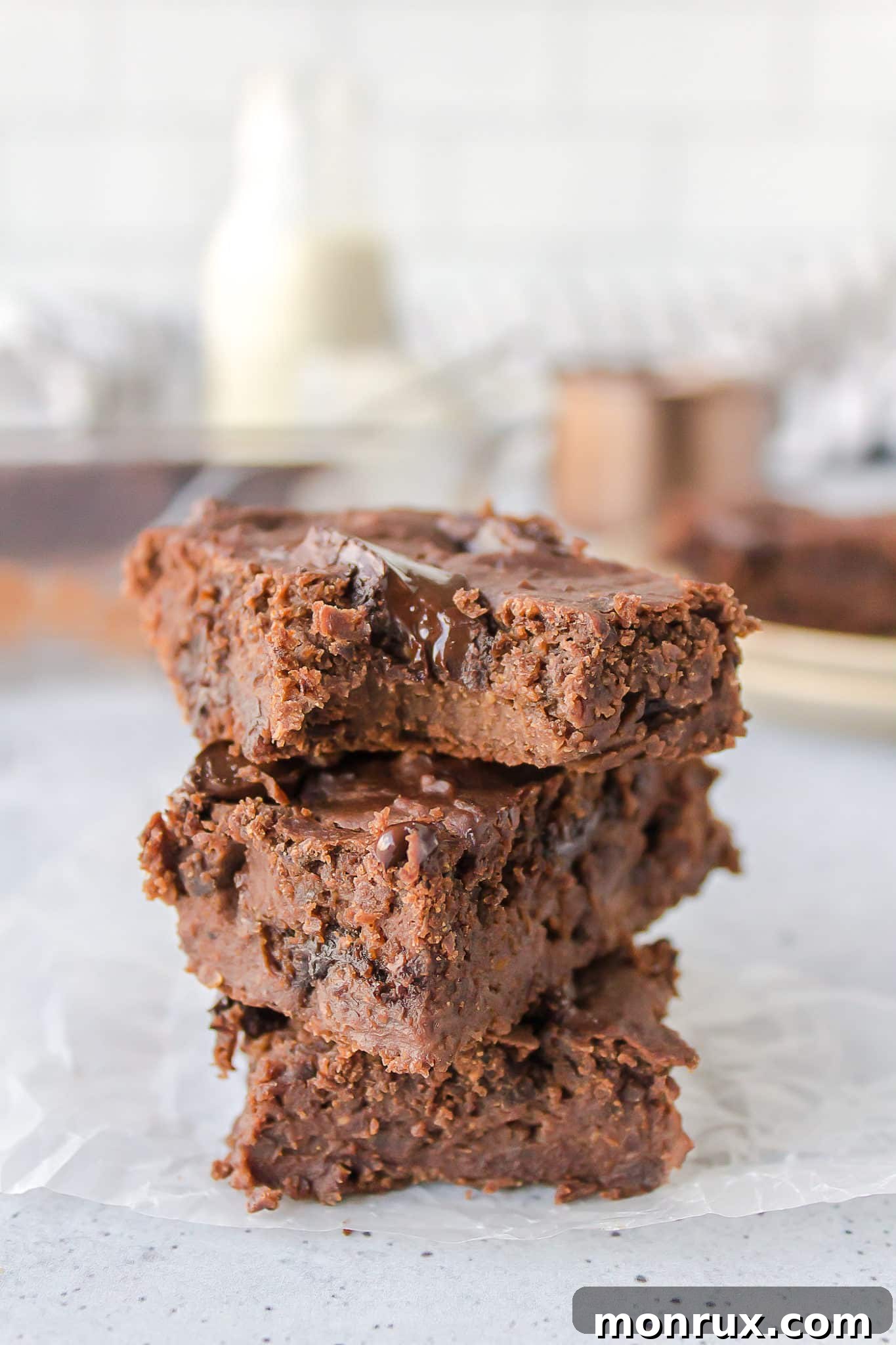 Stack of fudgy vegan black bean brownies on a rustic wooden table, garnished with a sprinkle of cocoa powder.