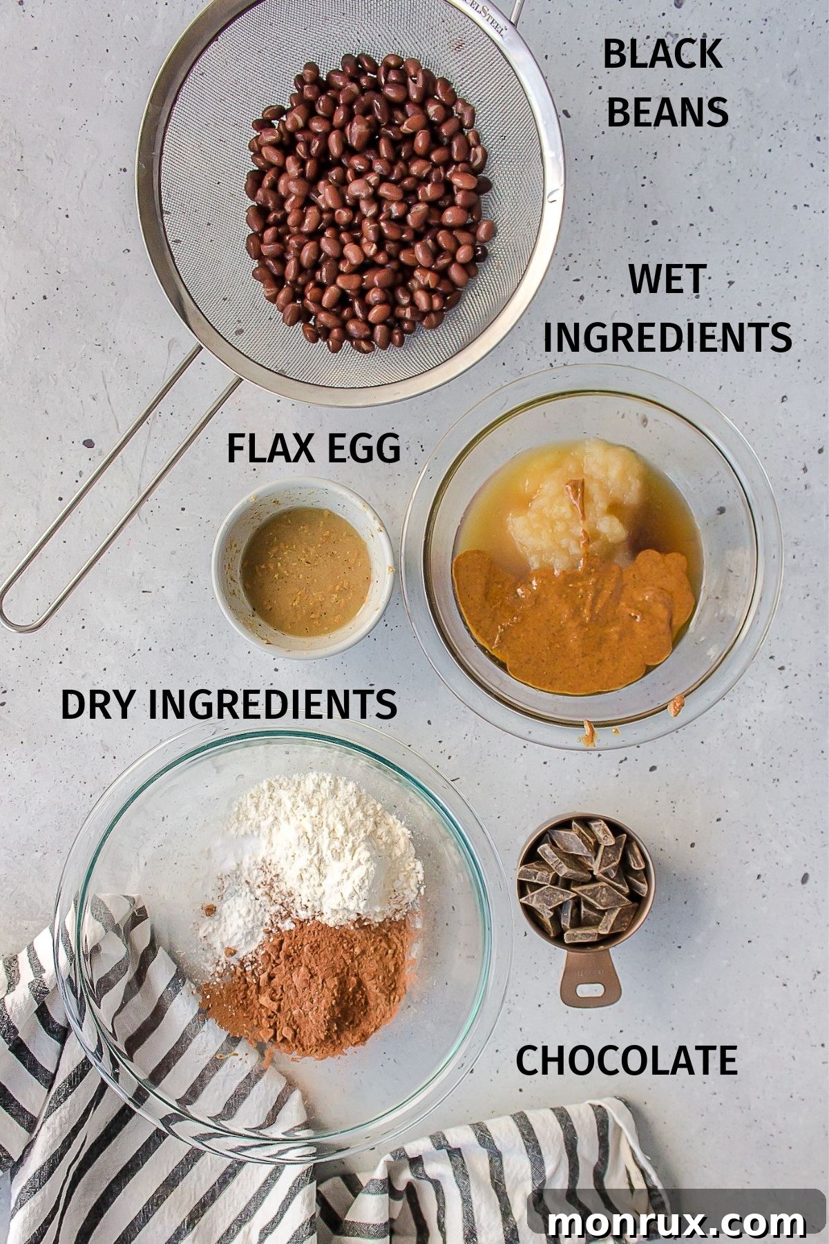 Collection of key ingredients for vegan black bean brownies, including canned beans, nut butter, maple syrup, and cocoa powder.