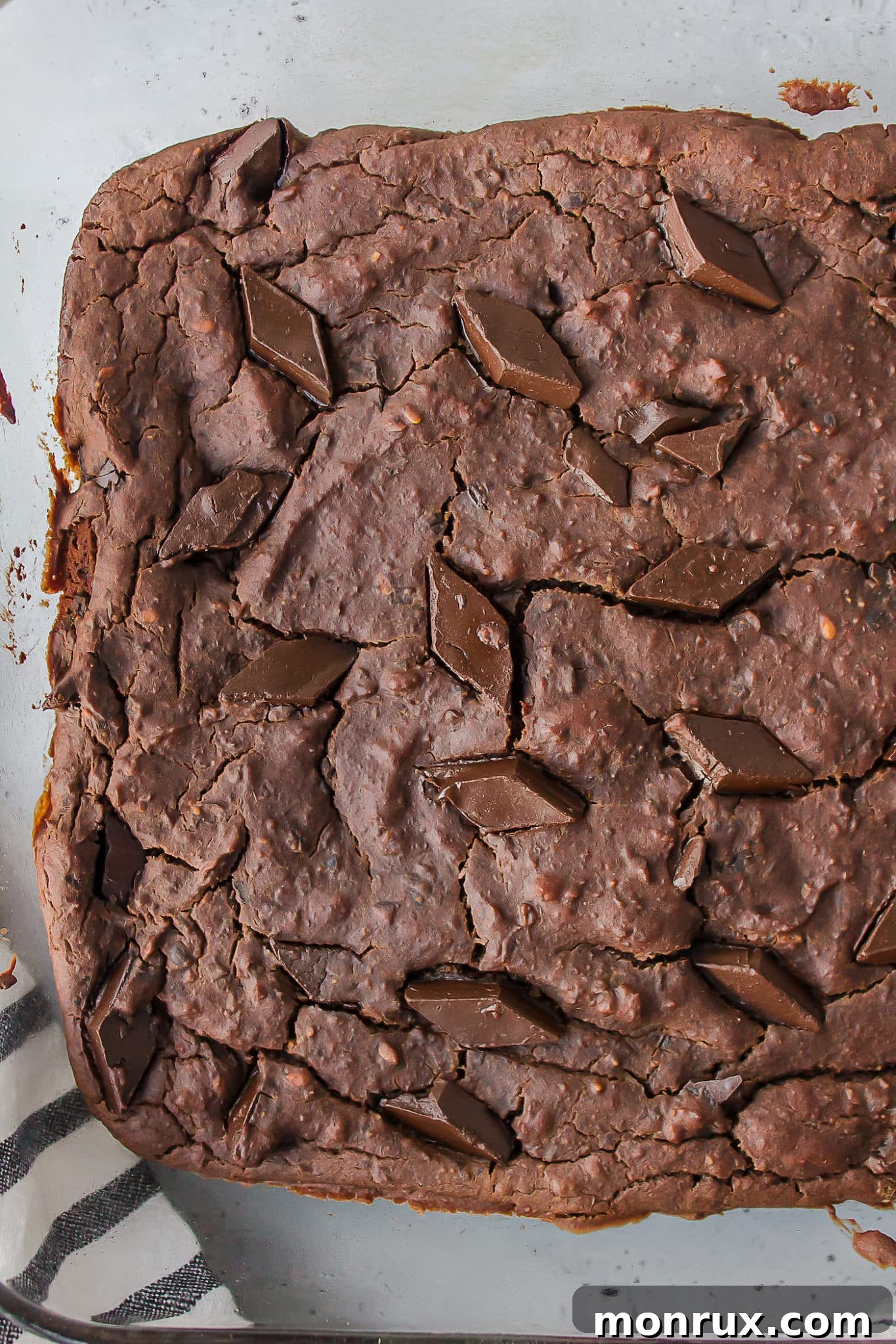 Freshly baked vegan black bean brownies cooling in a square baking dish, topped with melted chocolate chips.