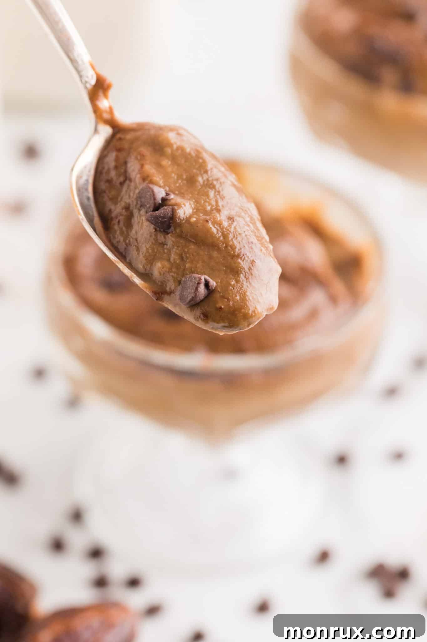 A spoon lifted from a white bowl, holding a perfect bite of creamy avocado chocolate pudding adorned with chocolate chips, ready to be savored.