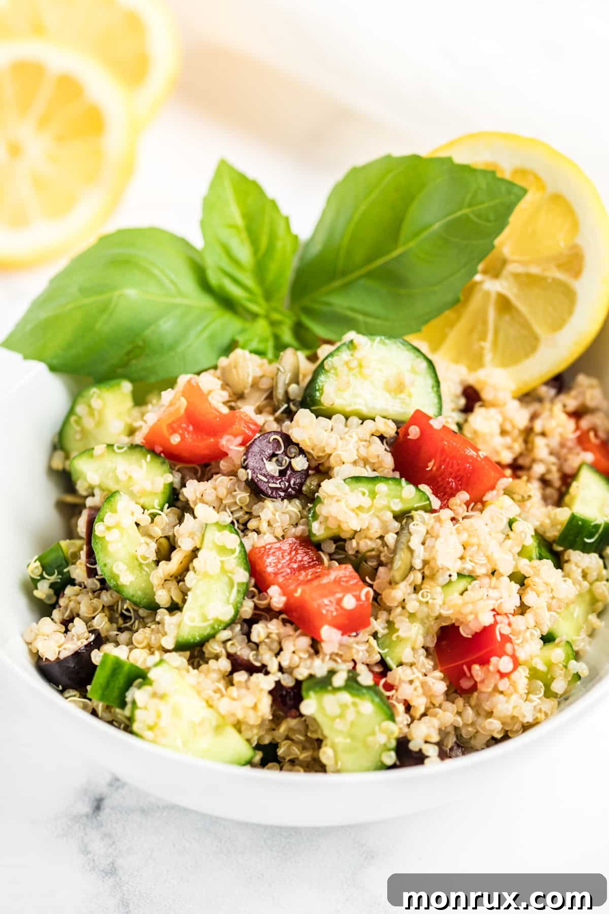 A bowl of quinoa salad with cucumbers, red pepper, and olives.