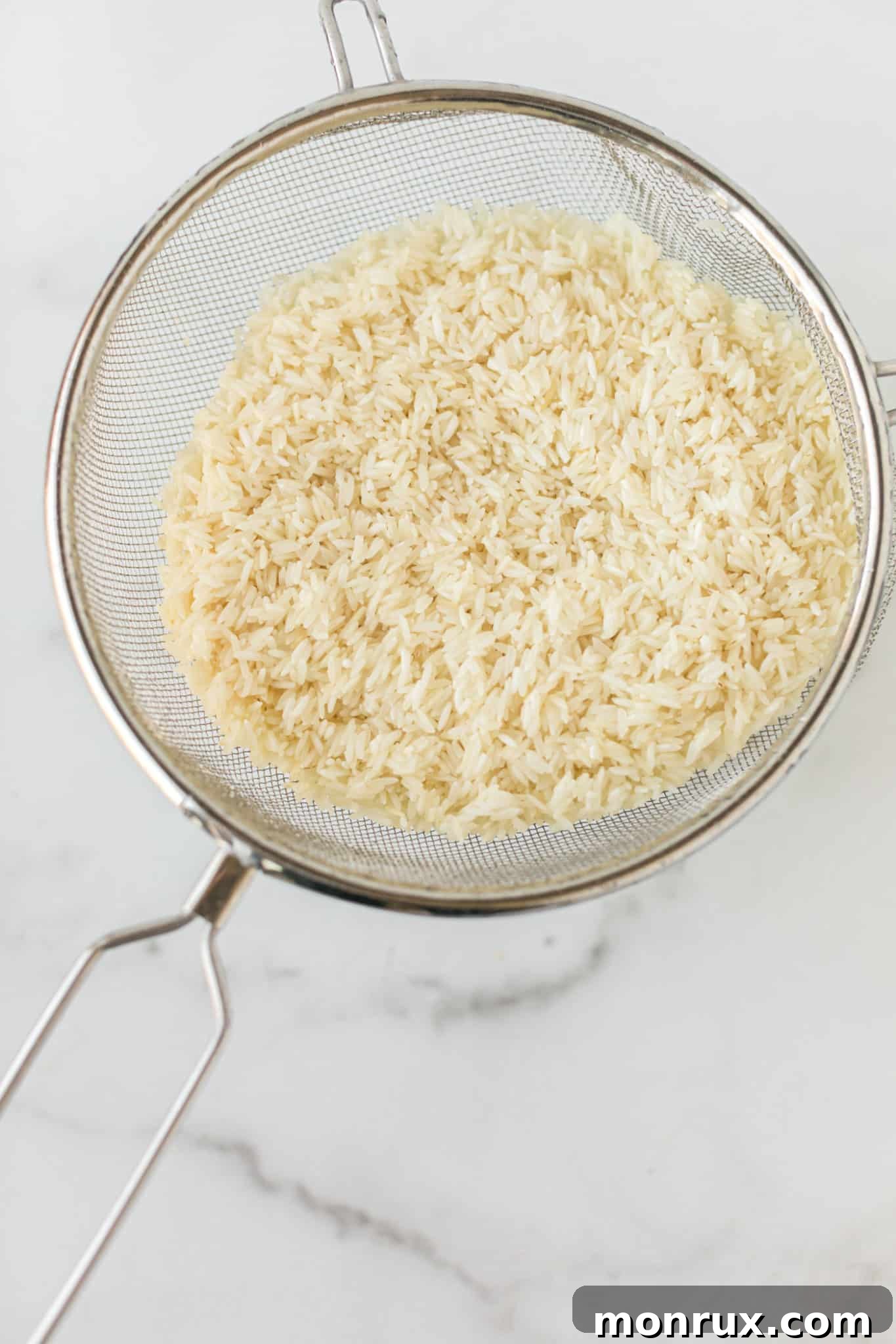White rice being rinsed in a fine-mesh colander under running water.