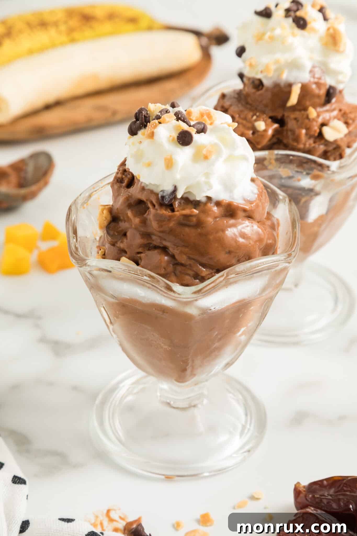 Scoops of creamy Chocolate Peanut Butter Banana Ice Cream served in sundae glasses, garnished with chocolate shavings and a hint of fresh mint.